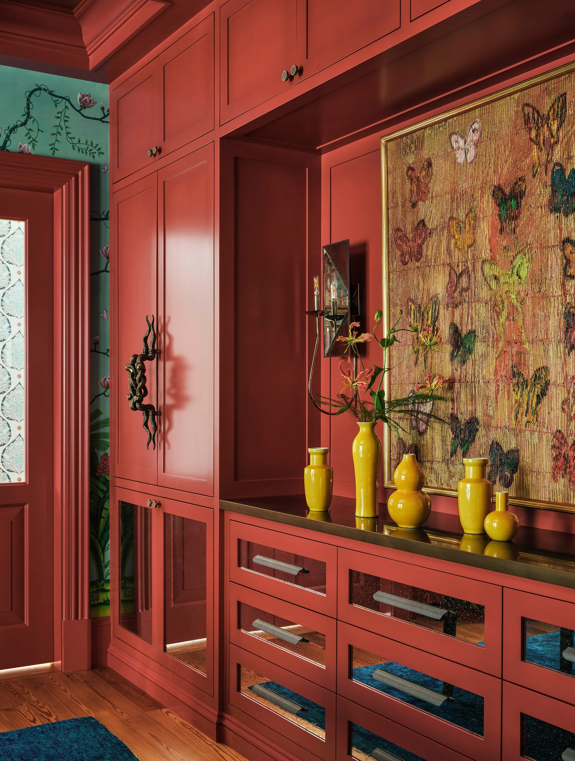 Deep red built-in cabinets featuring a recessed display area with bright yellow ceramic vases and framed butterfly artwork.