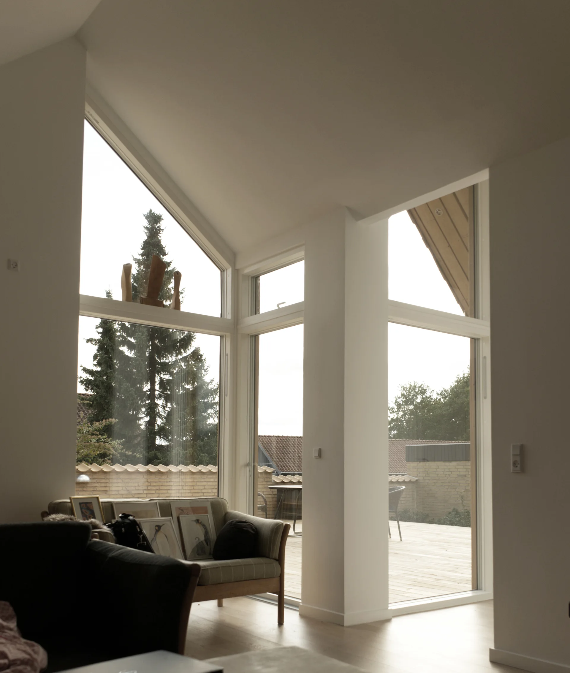 A bright living room features a patterned sofa placed near large angled windows that look out onto an outdoor wooden deck.