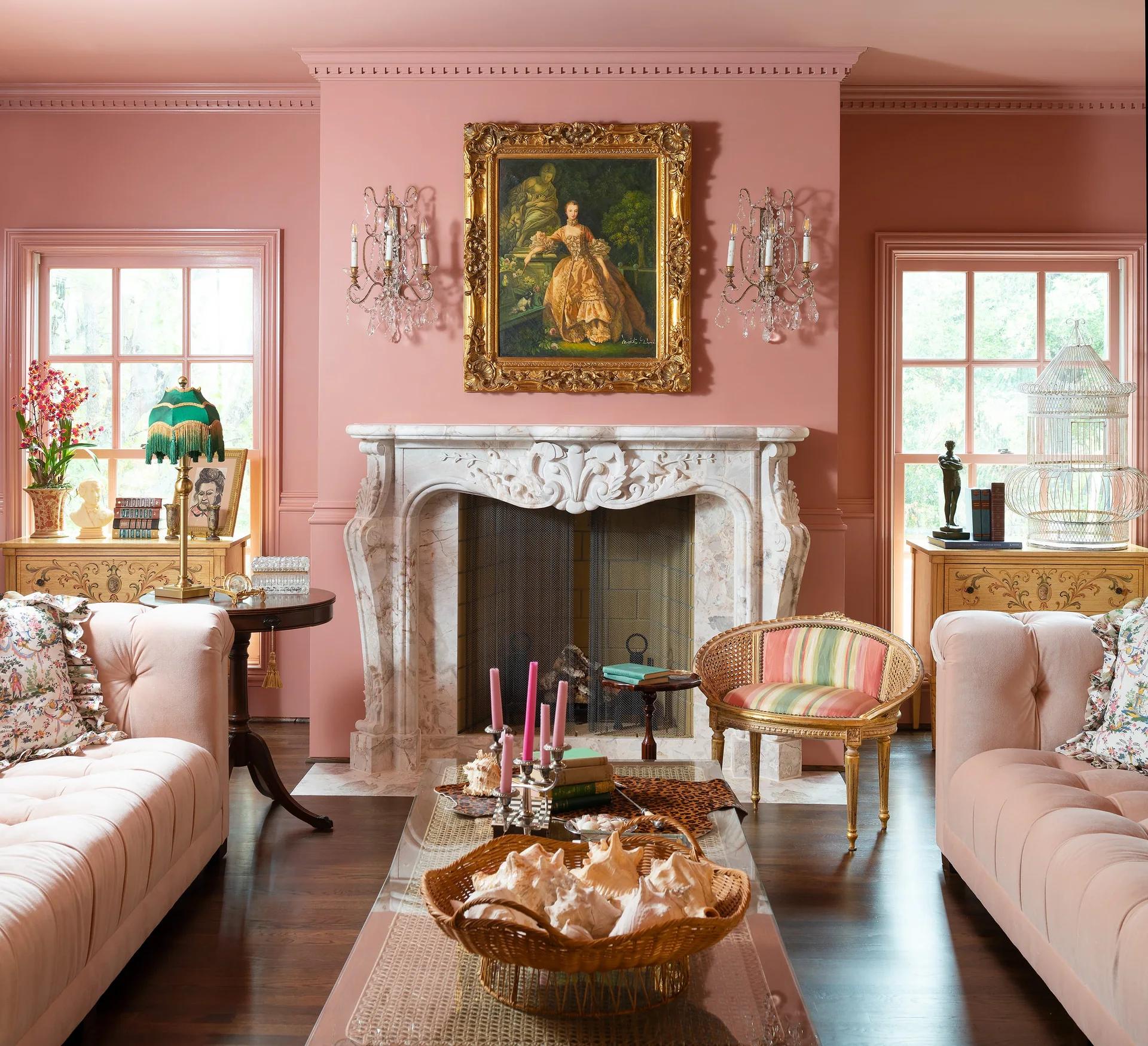 A formal pink living room featuring an ornate carved marble fireplace, matching pink tufted sofas, and crystal wall sconces.