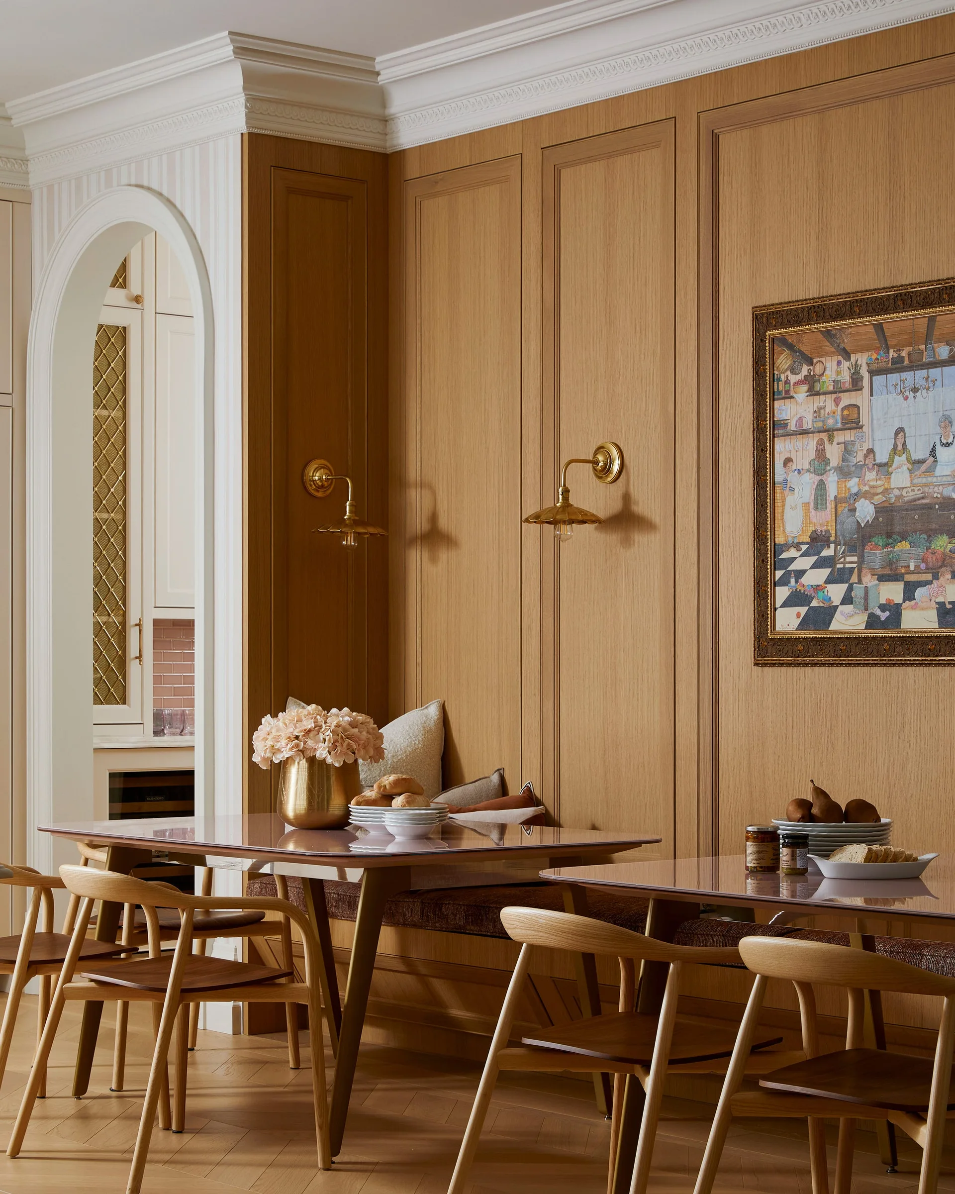A dining space with floor-to-ceiling vertical wood wall paneling, a built-in upholstered banquette, wooden chairs, and brass wall sconces.