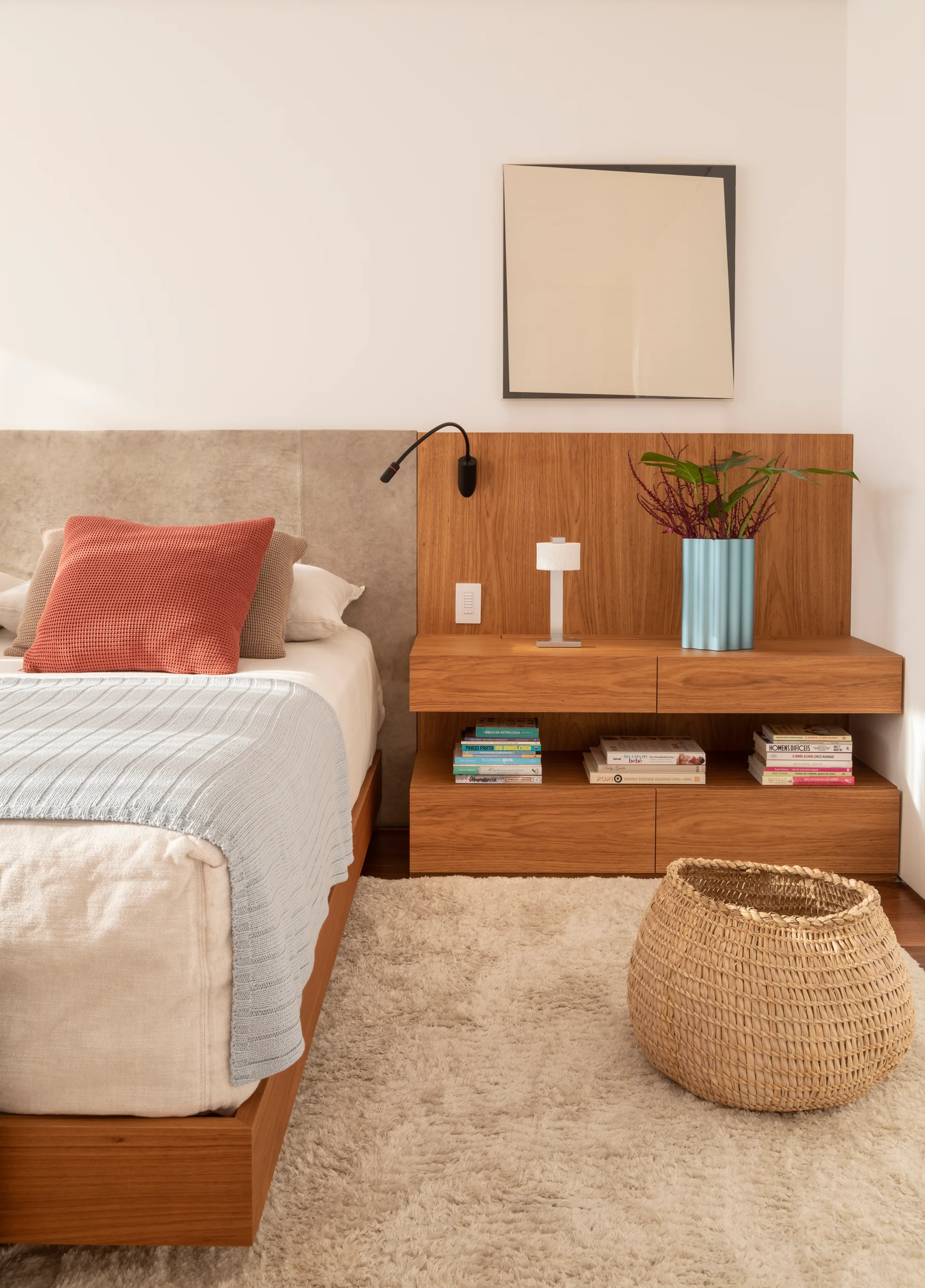 A modern bedroom features a wooden bed, an integrated oak headboard and floating nightstand, a soft shag rug, and a woven floor basket.
