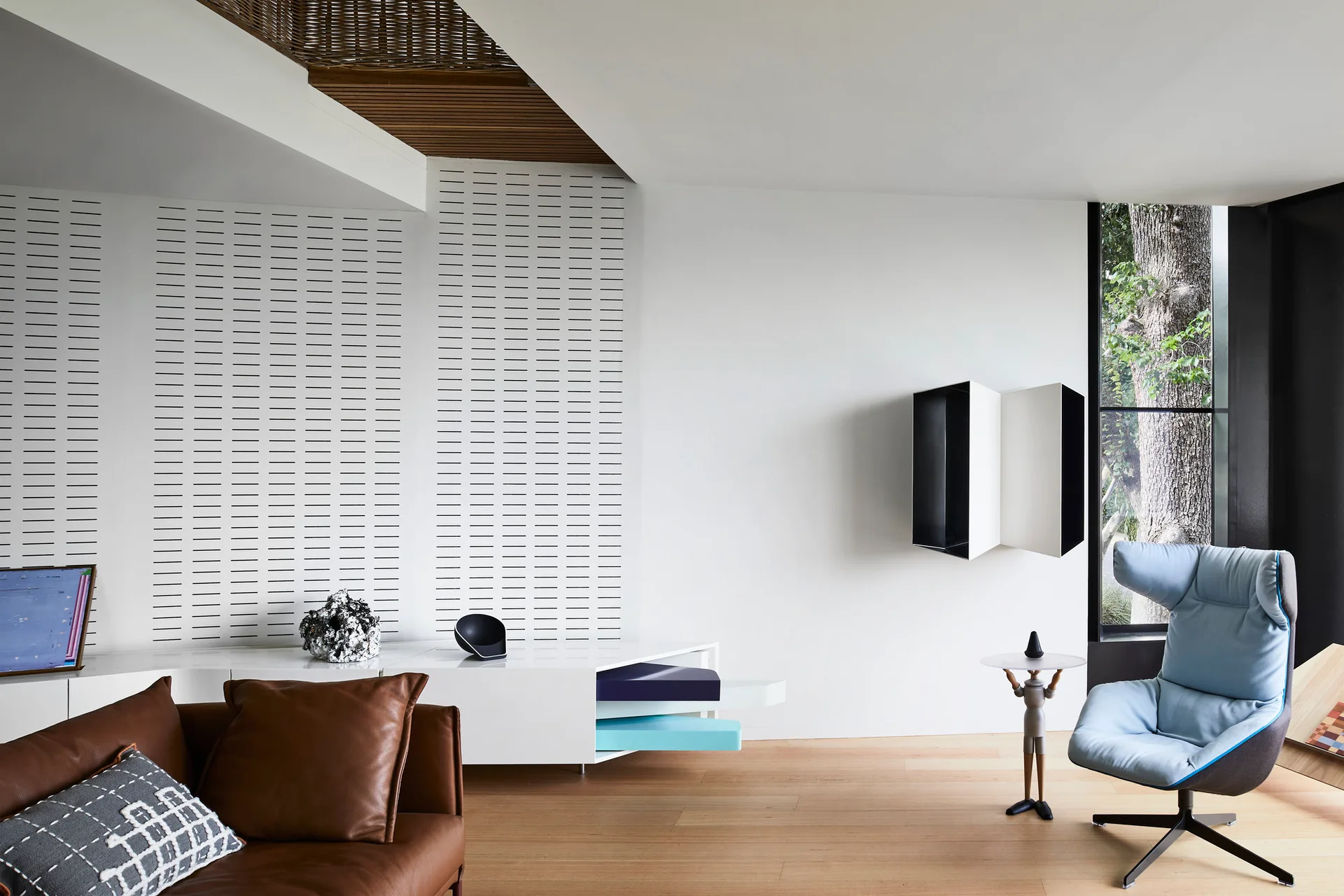 A modern living room featuring a brown leather sofa, a light blue armchair, and a white accent wall with horizontal slotted panels.