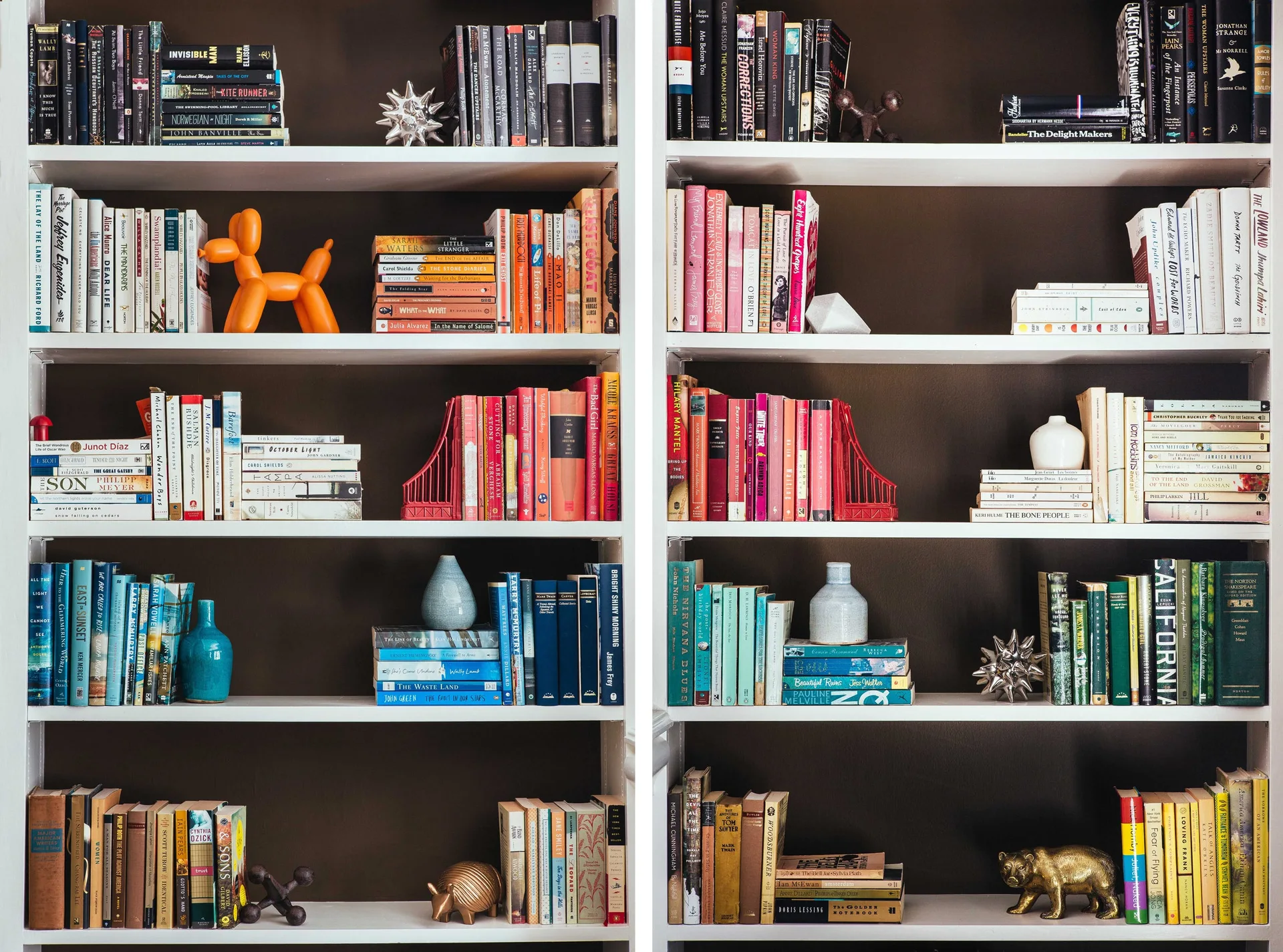A white built-in bookshelf with books organized by spine color on several shelves against a dark brown wall, decorated with small sculptures.
