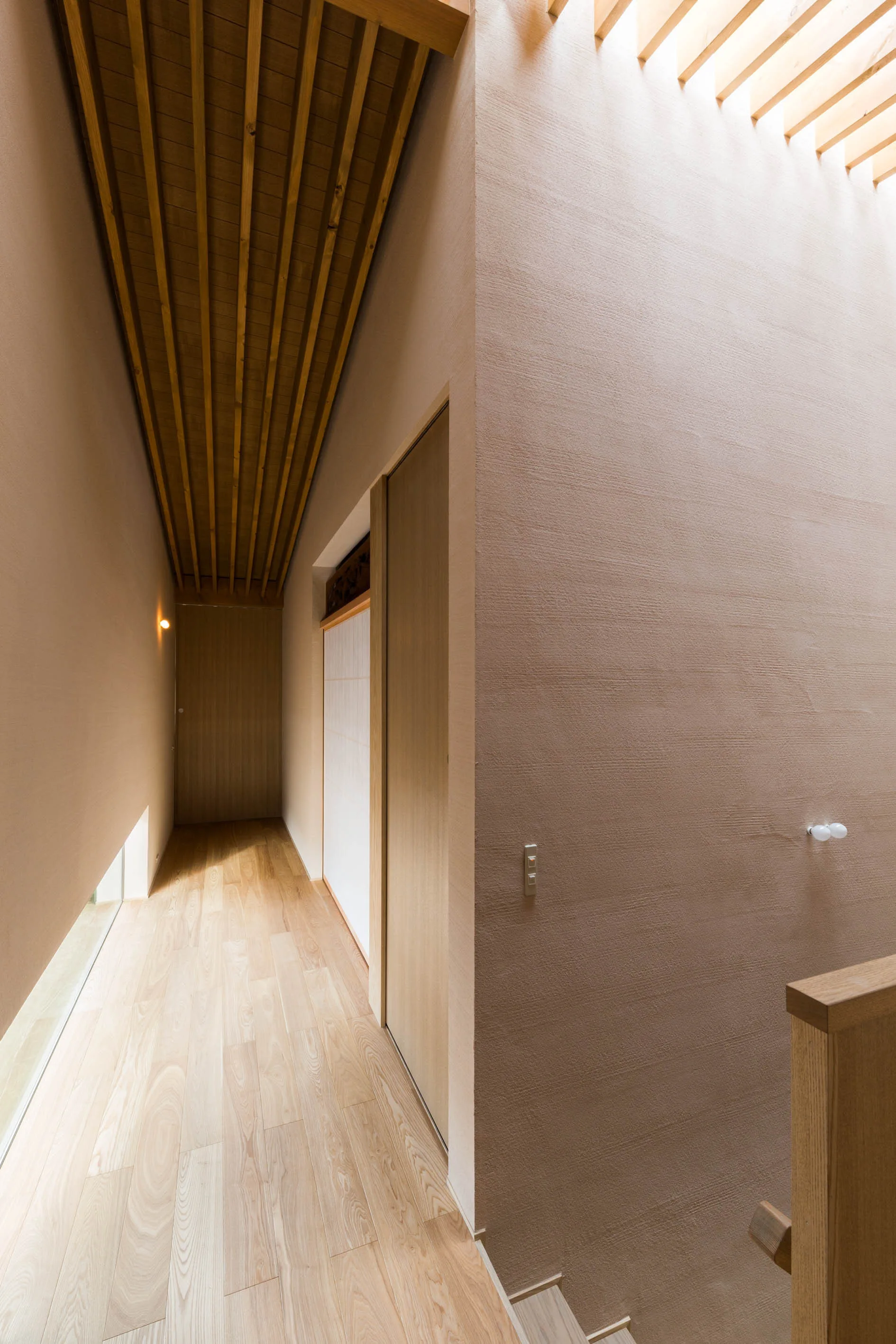 Minimalist hallway featuring textured beige plaster walls, a wooden slatted ceiling, and light hardwood floors.