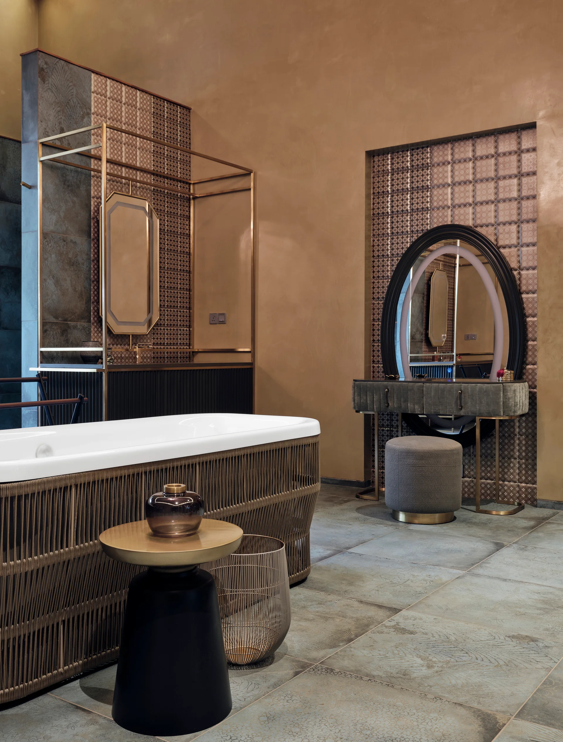 An earth-toned bathroom features a freestanding bathtub wrapped in textured rope, a recessed vanity niche with an oval mirror, and large floor tiles.