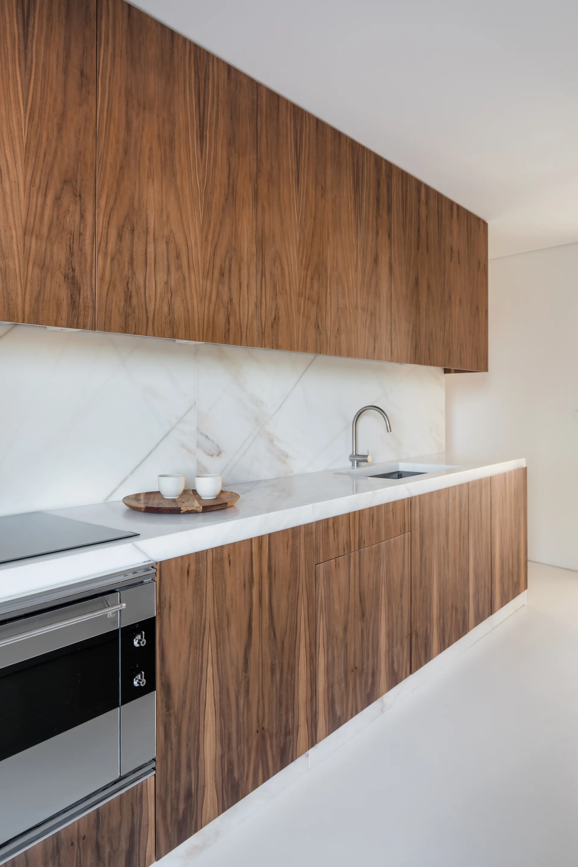 Modern kitchen featuring flat-front wood cabinets, a veined white stone countertop and slab backsplash, an undermount sink, and a built-in oven.