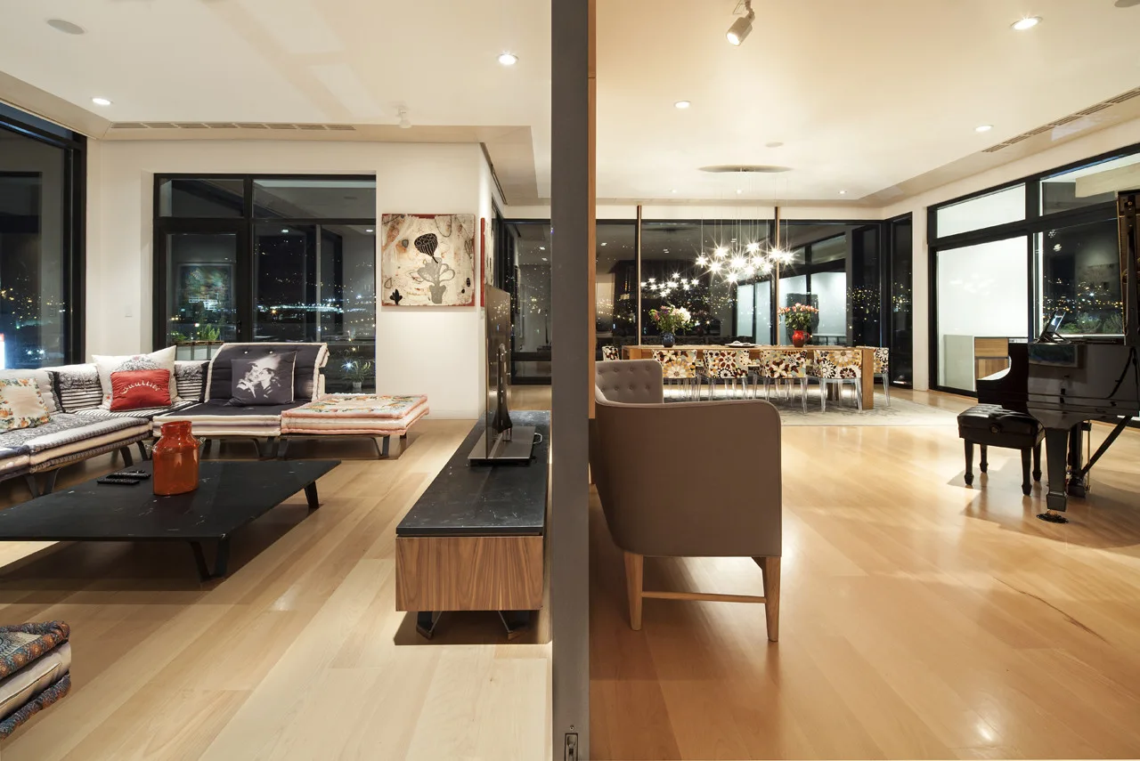 An open-concept living space with a modern sectional sofa, a black console, a grand piano, and a dining table under a pendant light at night.