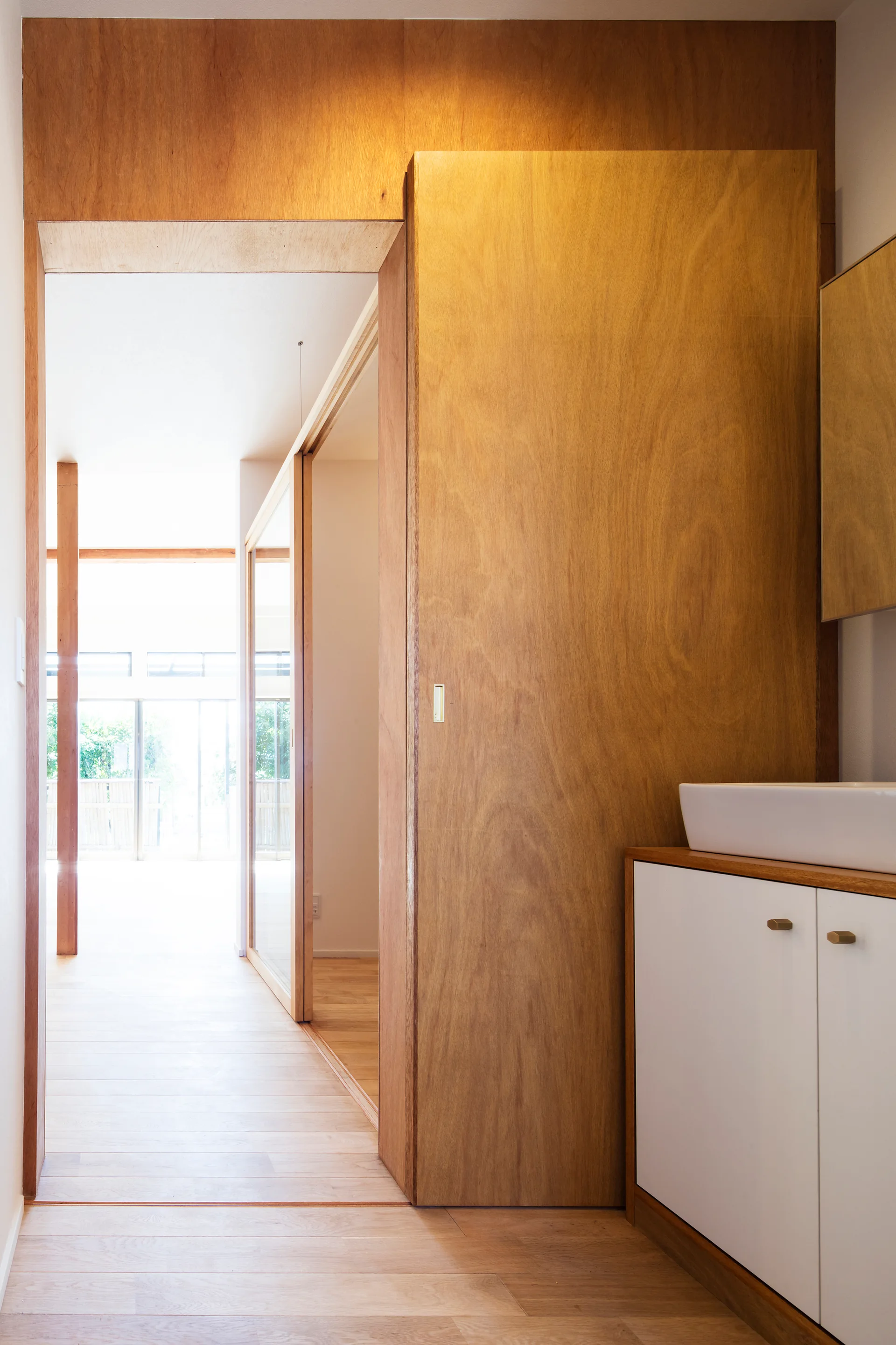 A bright hallway features light wood floors, a large plywood sliding door, and a white bathroom vanity with a ceramic vessel sink.