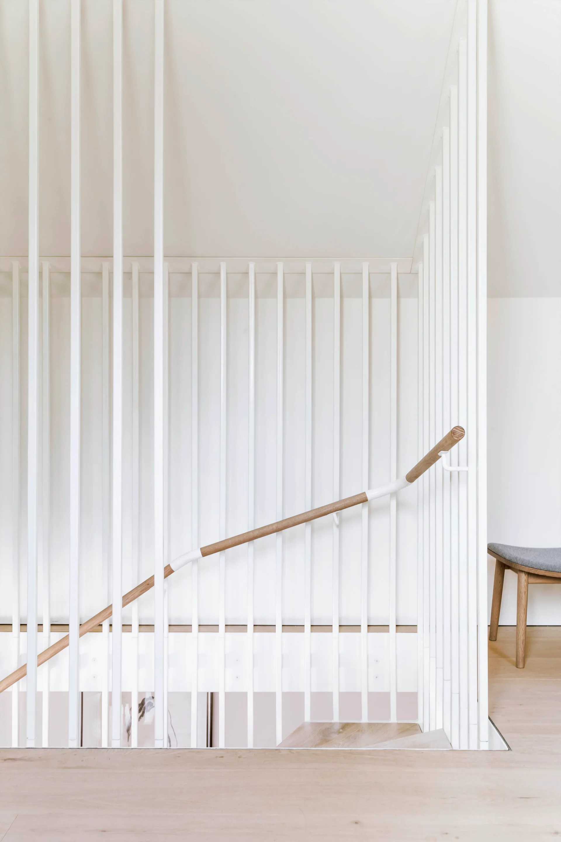 A minimalist staircase features floor-to-ceiling white vertical balusters, a smooth wooden handrail, and light hardwood flooring.