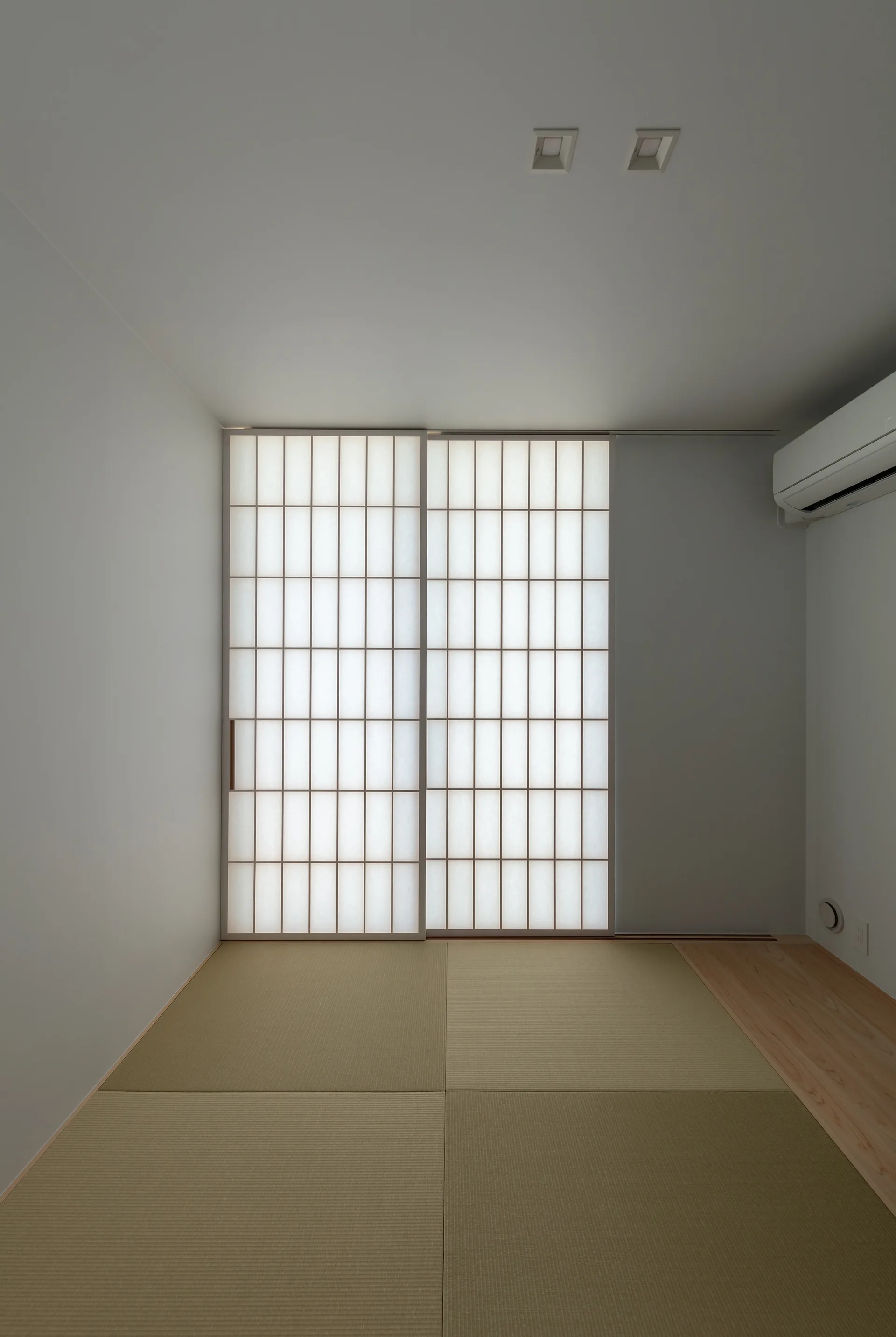 A minimalist Japanese room featuring traditional straw-textured tatami floor mats and translucent white shoji sliding doors under a plain ceiling.