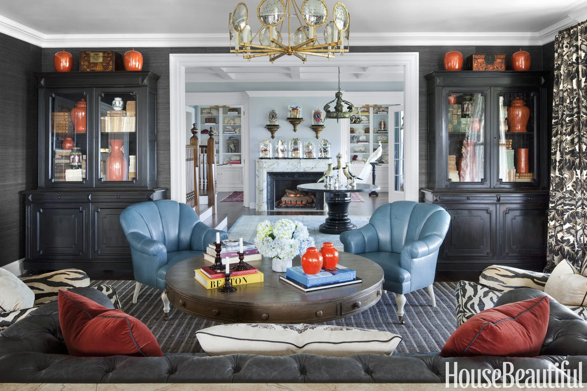 A symmetrical living room features two black display cabinets, a pair of blue leather armchairs, and a round wooden coffee table on a patterned rug.