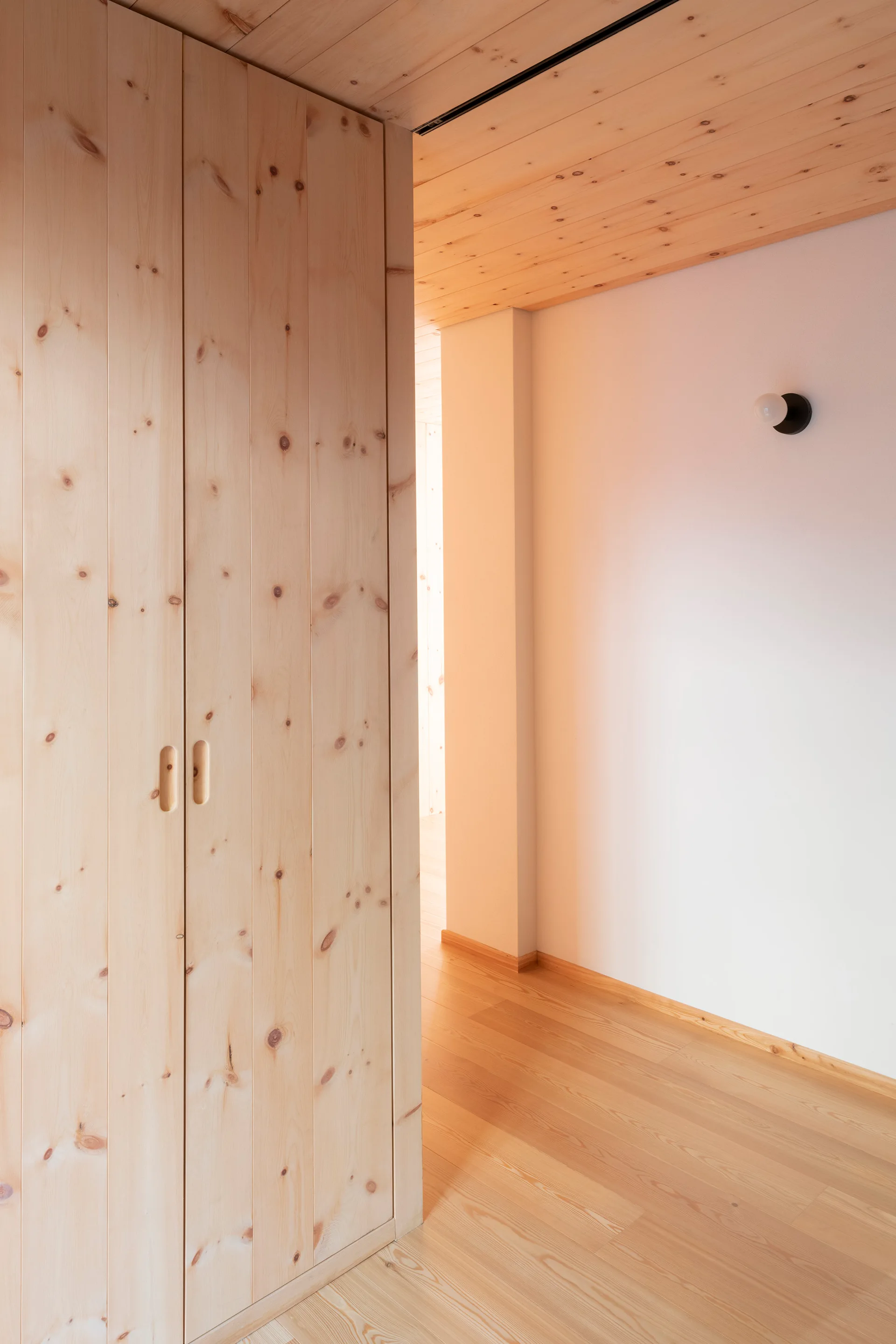 A bright hallway featuring floor-to-ceiling knotty wood cabinets, matching wood plank ceilings and floors, and a minimalist wall sconce.