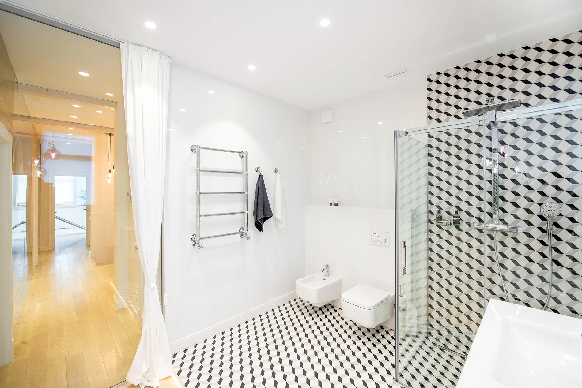 A modern white bathroom featuring black and white geometric cube floor tiles, a glass shower, and a wall-hung toilet and bidet.