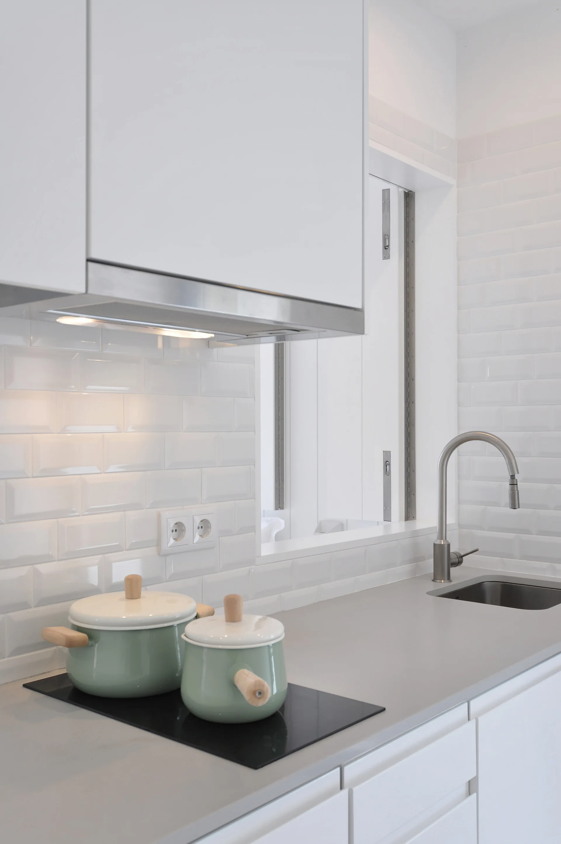 A modern kitchen featuring white subway tile, light gray countertops, an undermount sink, and two sage green pots on an induction cooktop.