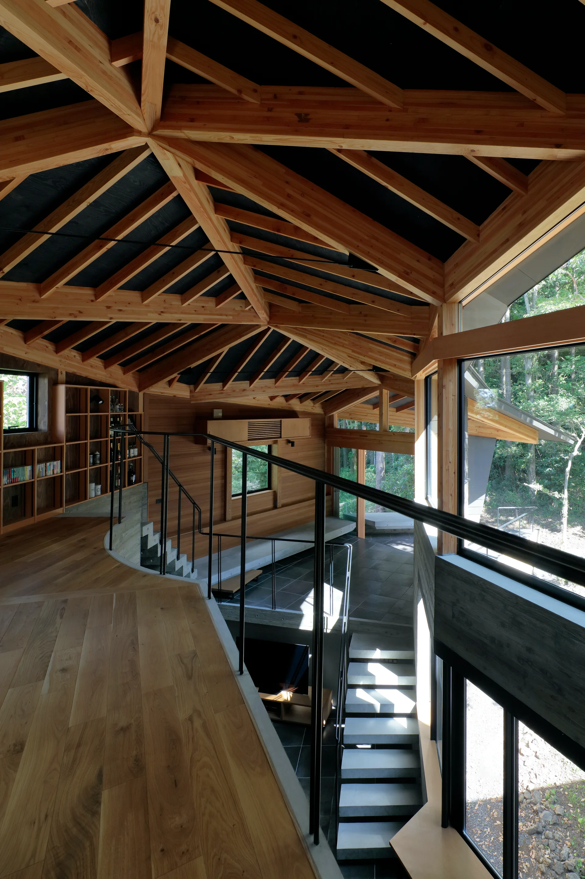 A modern split-level interior featuring a curved wooden hallway with a black railing, concrete stairs, and an intricate exposed timber ceiling.