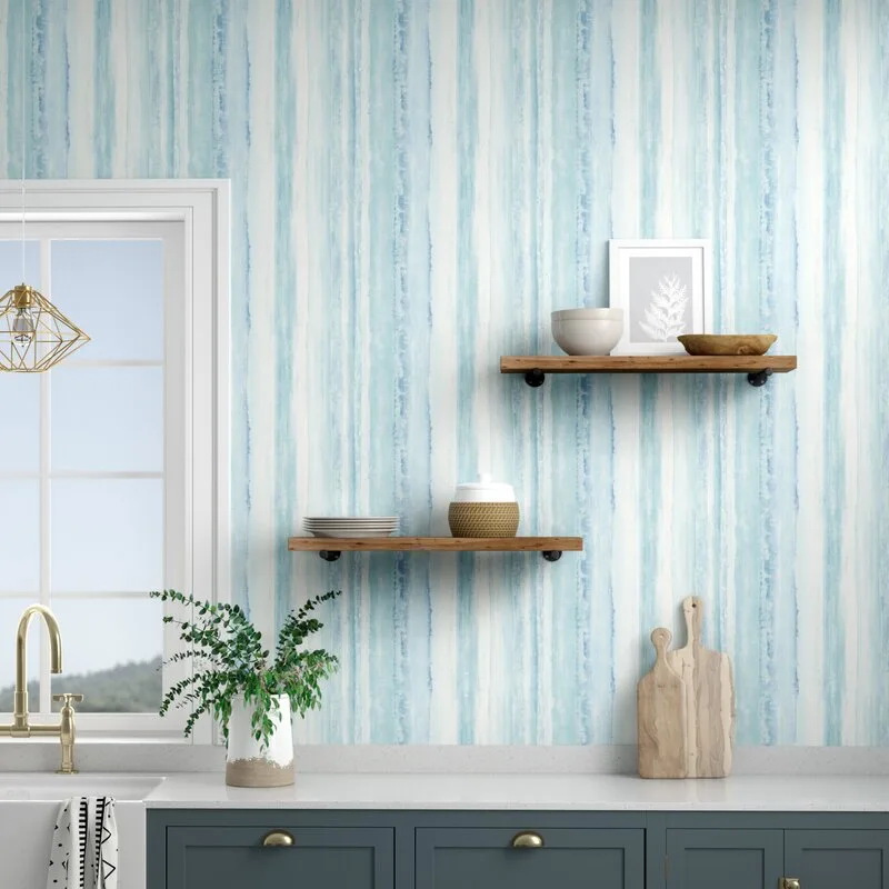 A kitchen featuring blue watercolor striped wallpaper, dark blue base cabinets with brass hardware, and two staggered floating wood shelves.