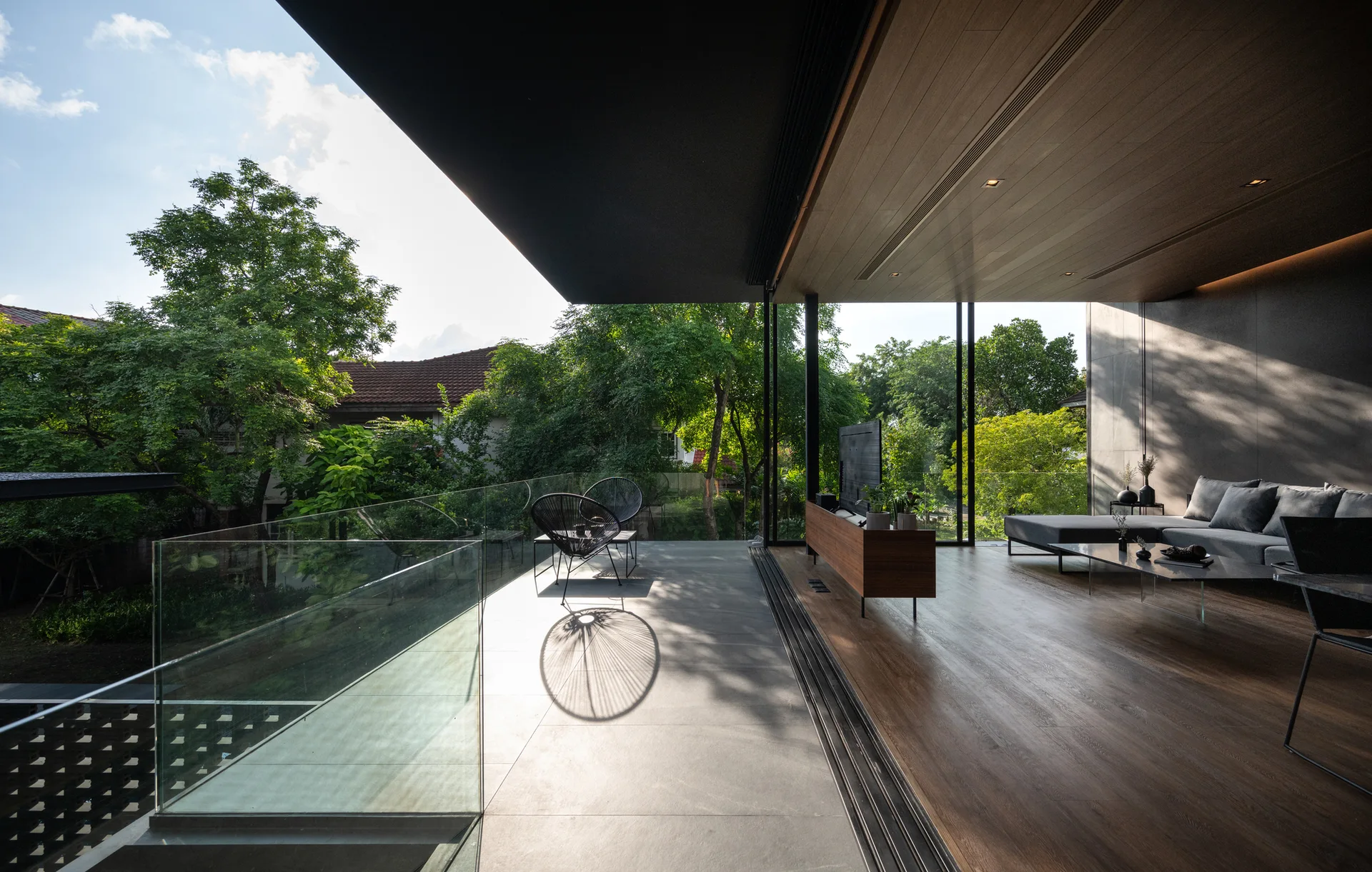 A contemporary indoor-outdoor living room features a wood-paneled ceiling, a grey sectional sofa, and sliding glass doors that open to a concrete terrace.