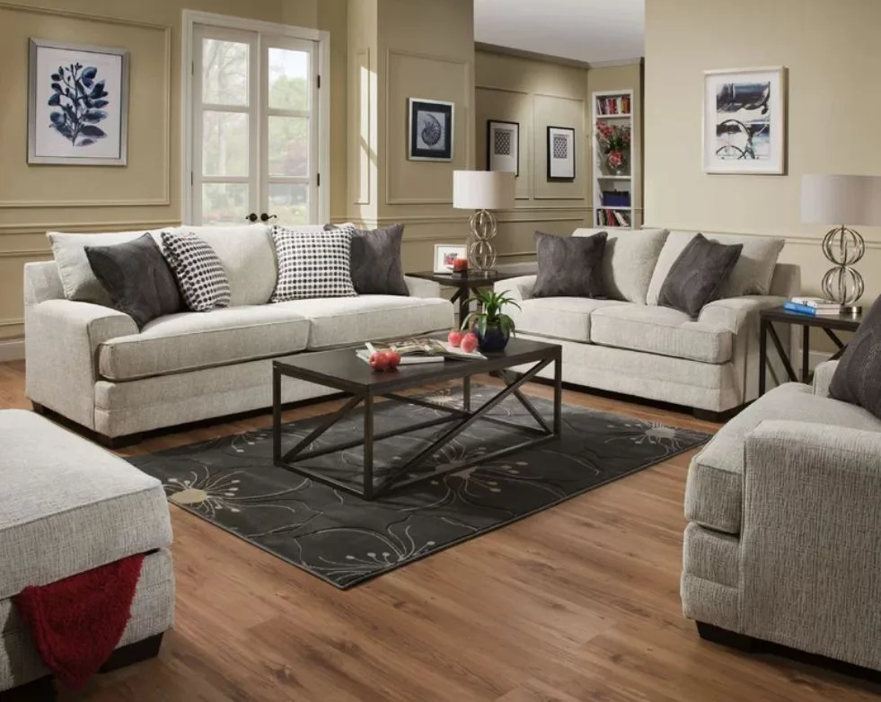 Two light grey upholstered sofas surround a dark metal coffee table on a floral patterned rug in a living room with beige paneled walls.