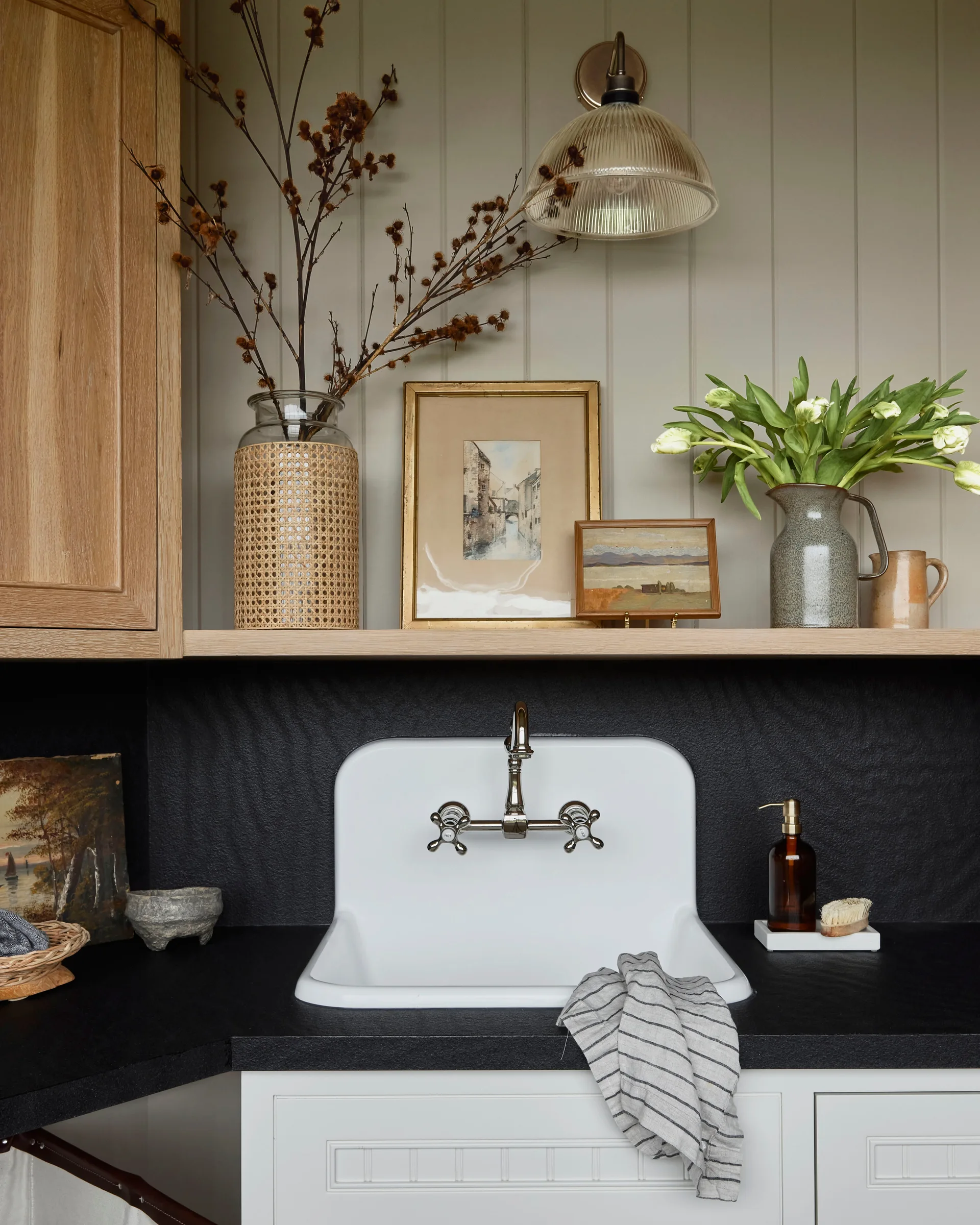 A wall-mounted utility sink with a chrome faucet is set against a black countertop under a wood shelf with decorative frames and vases.