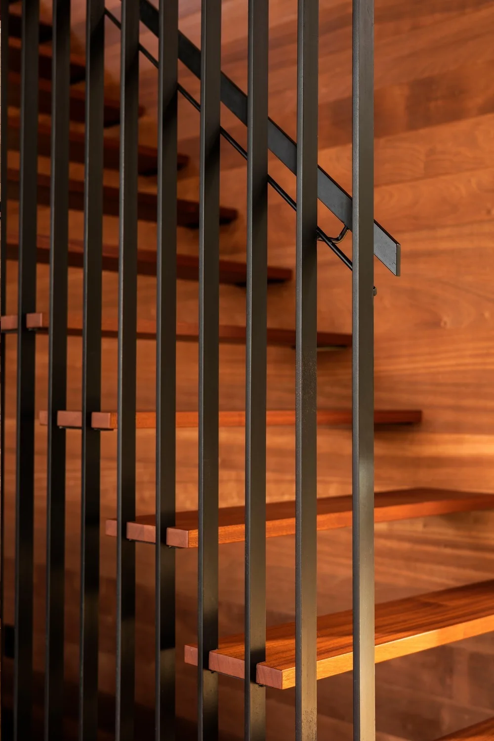 A modern staircase features open wooden treads, a vertical black metal railing, and a matching wood-paneled wall.
