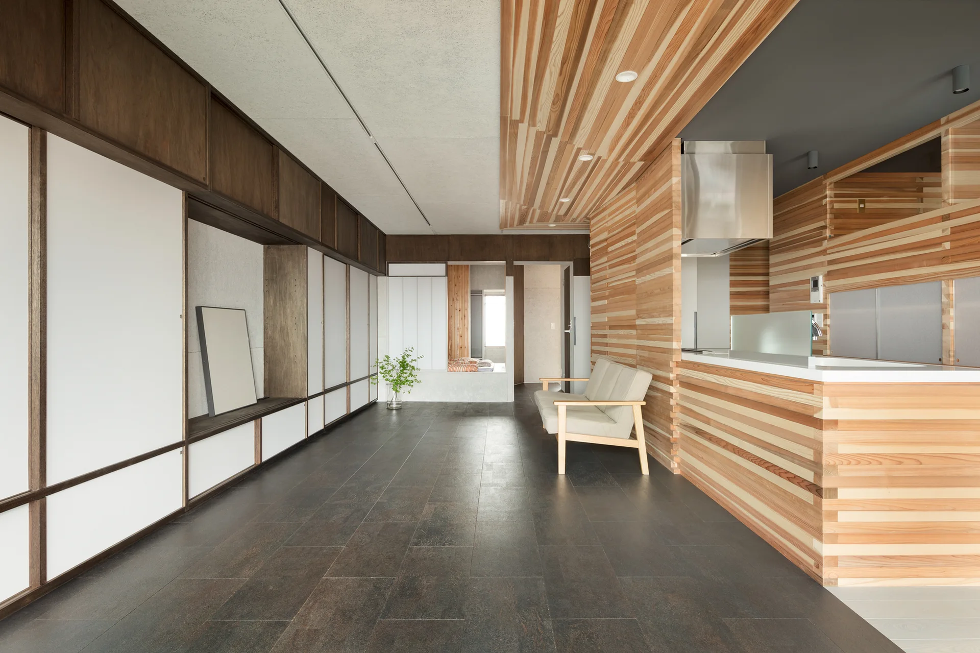 A minimalist living space featuring horizontal wood slat wall paneling, a beige sofa, dark floor tiles, and white built-in sliding cabinets.