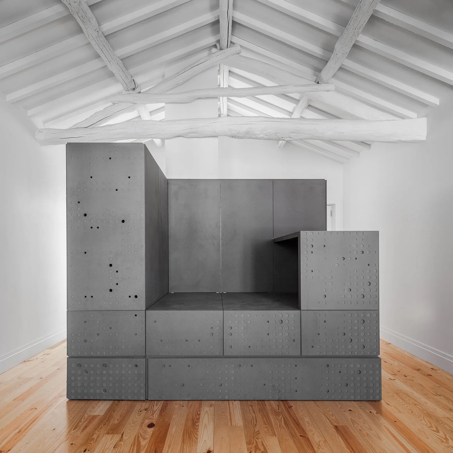 A large dark gray modular cabinet with perforated circle patterns stands on light wood floors under white painted ceiling rafters.
