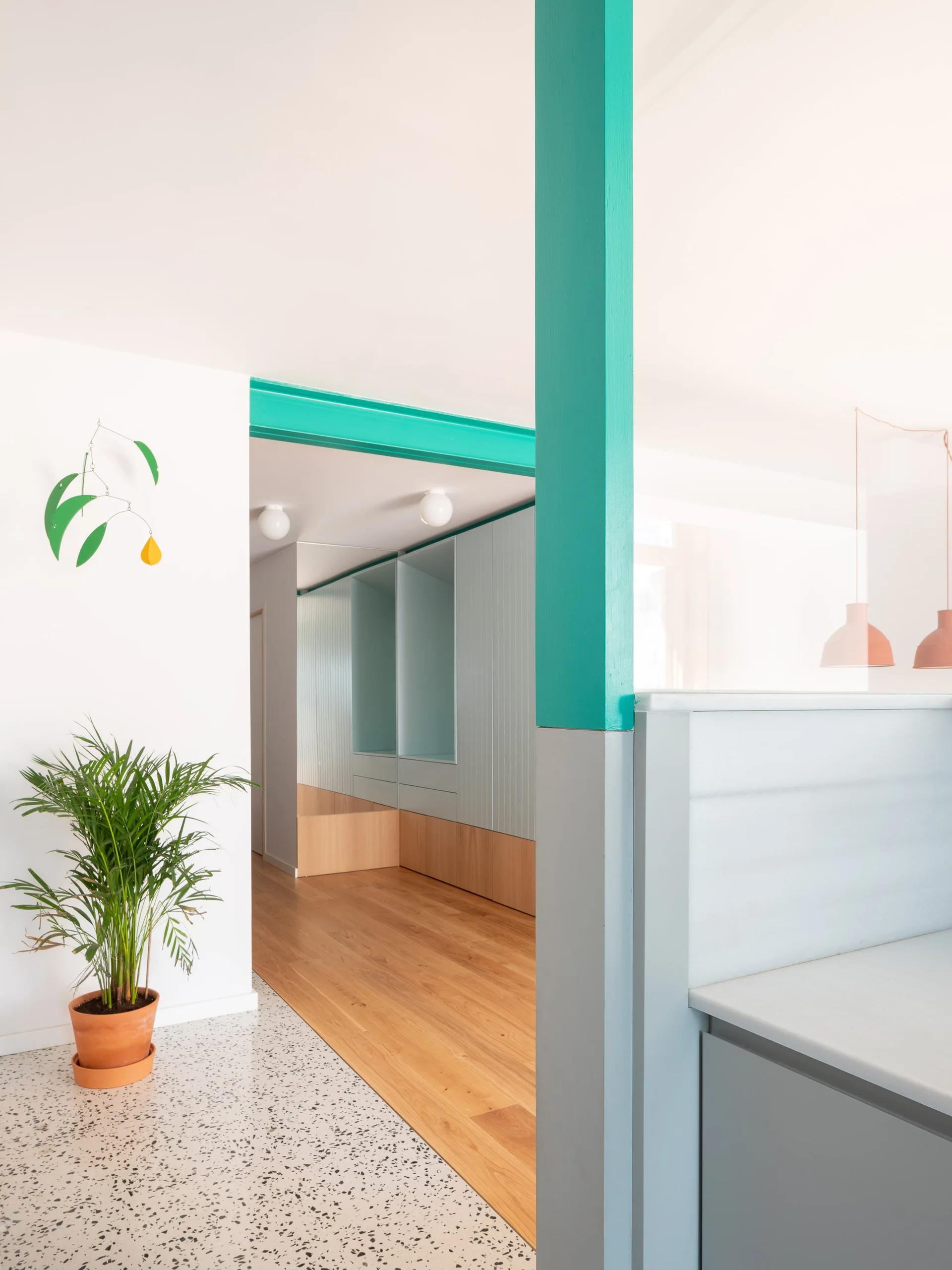 A bright hallway features light blue built-in cabinets, light wood flooring, a speckled terrazzo entryway, and a bold teal column.