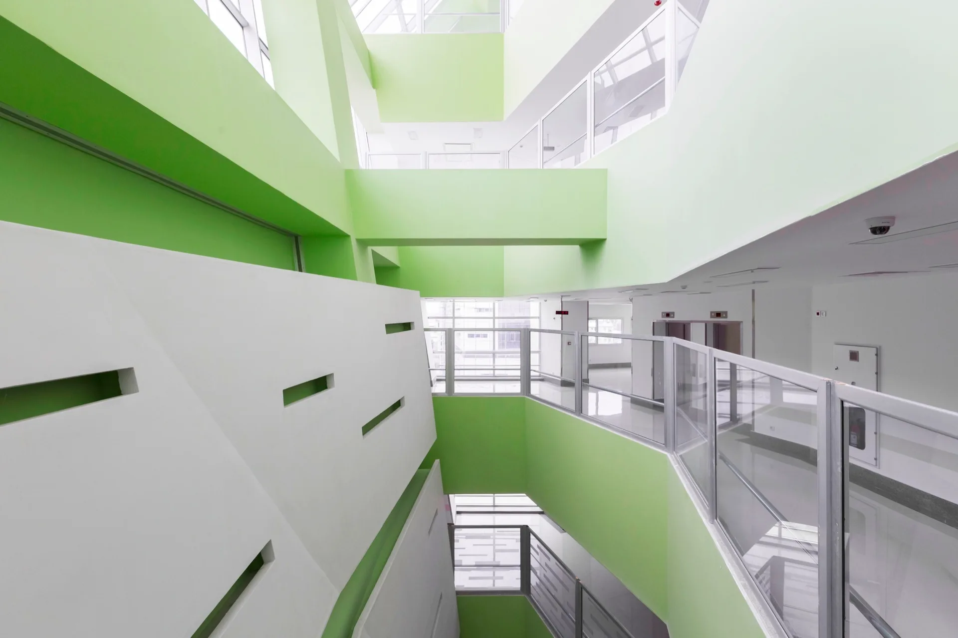 A modern multi-level interior atrium featuring bright green and white walls, glass railings, and rectangular geometric cutouts.
