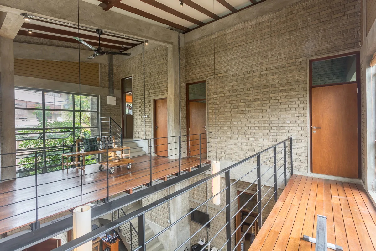 An industrial loft mezzanine features warm wood plank flooring, black steel safety railings, and walls made of light-colored exposed brick.