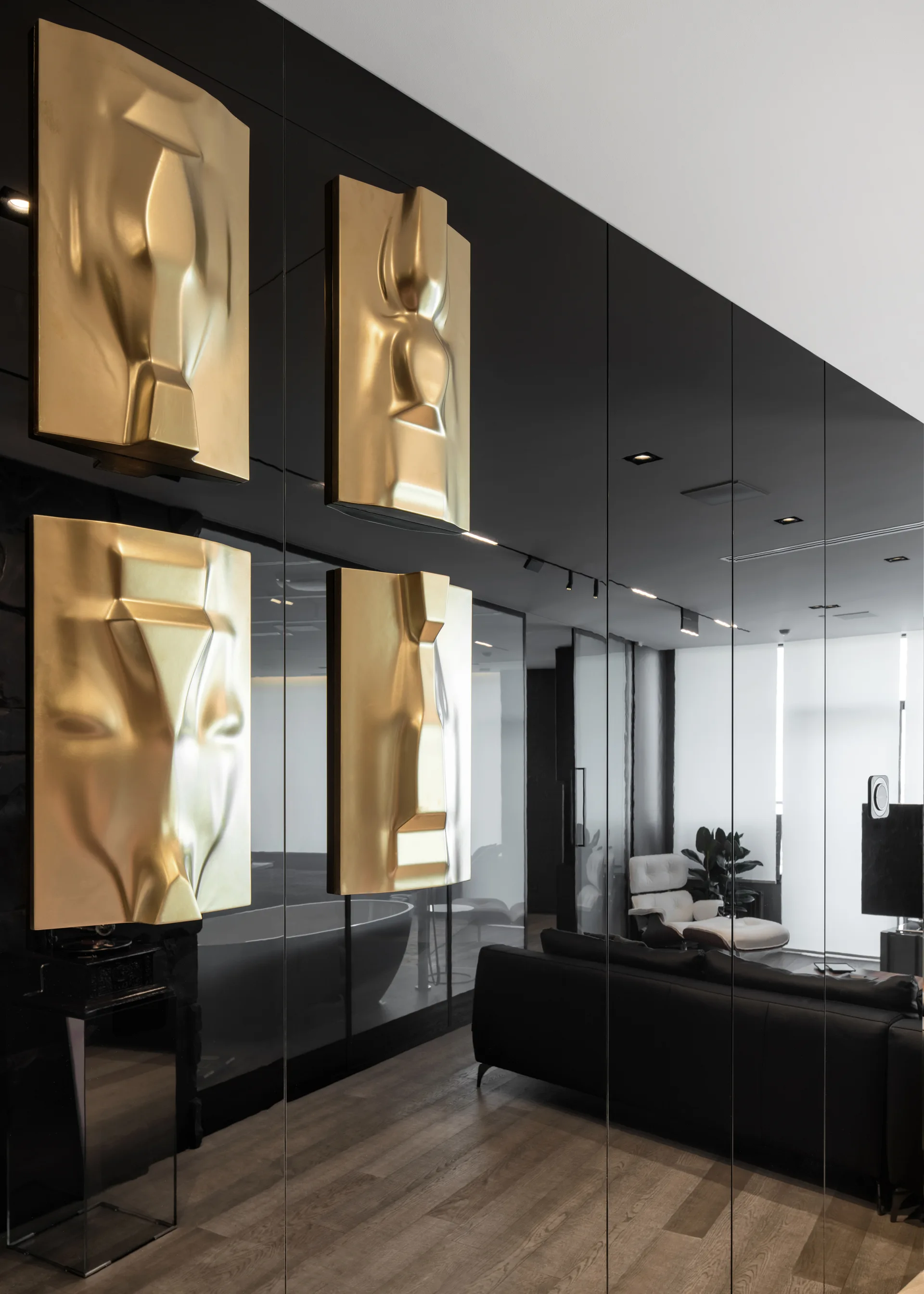A modern living room features glossy black mirrored wall panels adorned with four gold relief sculptures reflecting a black sofa.