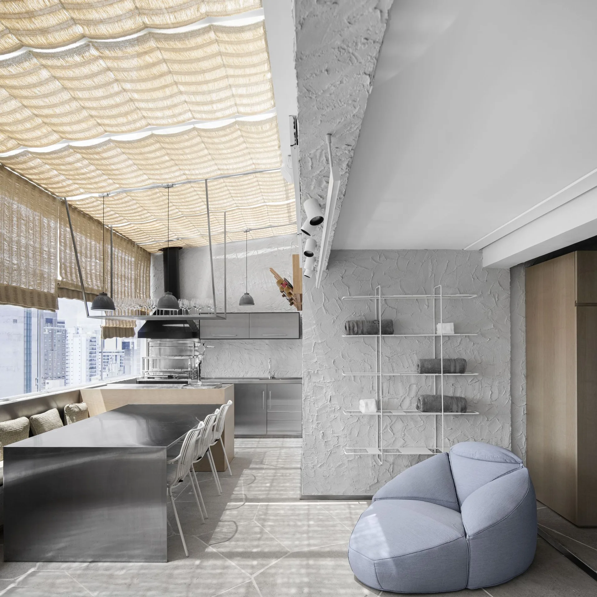 A modern open-concept kitchen and dining area features a stainless steel table, rough textured walls, and a draped fabric canopy ceiling.
