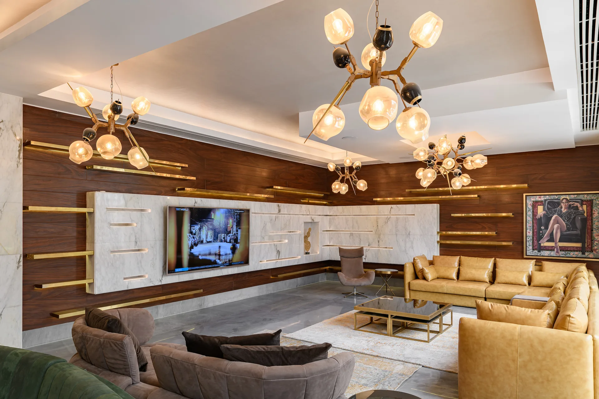 A contemporary living room featuring a tan leather sectional, wood-paneled walls with floating gold shelves, and a backlit white marble TV wall.