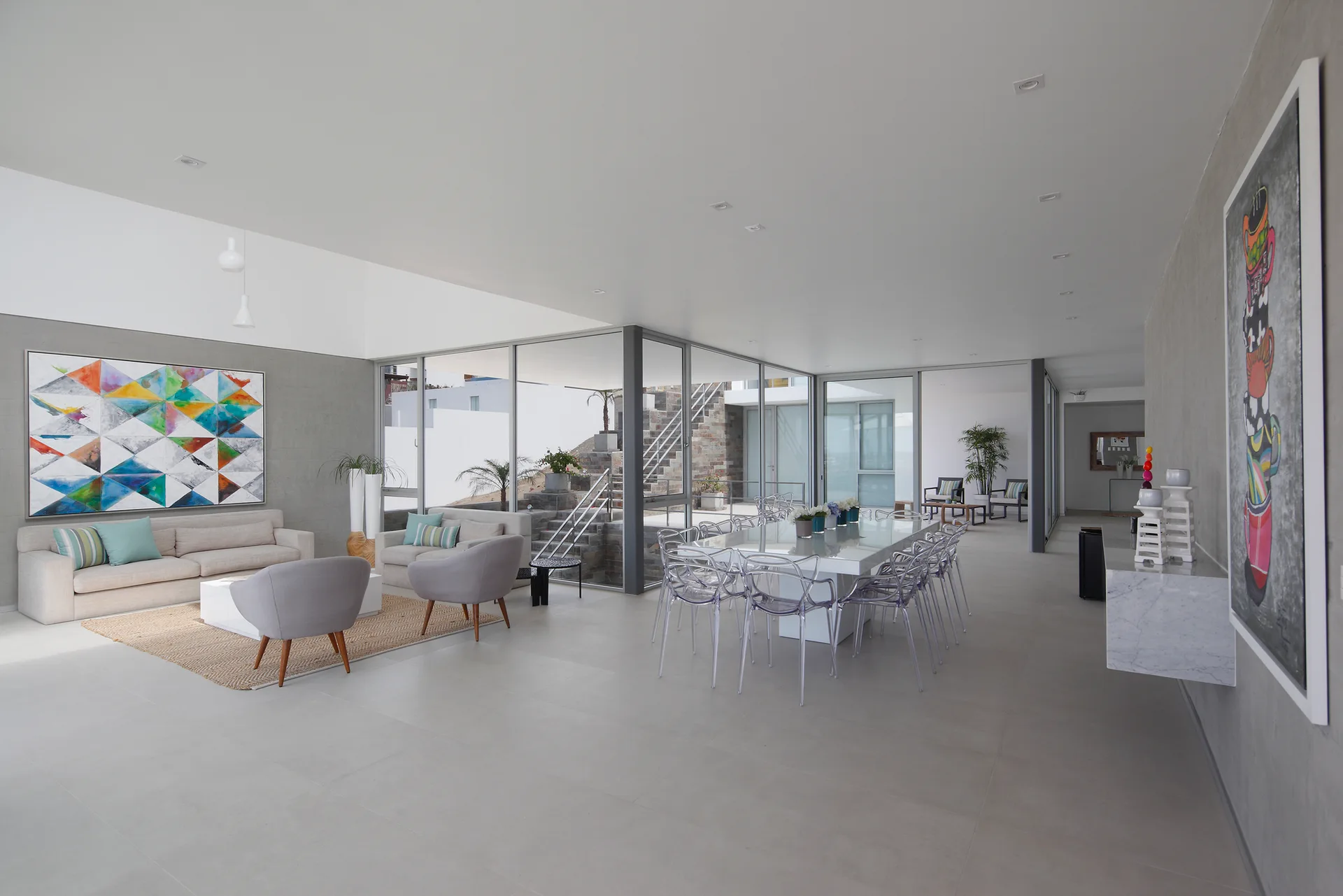 A spacious open-plan living and dining area features gray walls, a beige sofa, and transparent dining chairs around a white table.