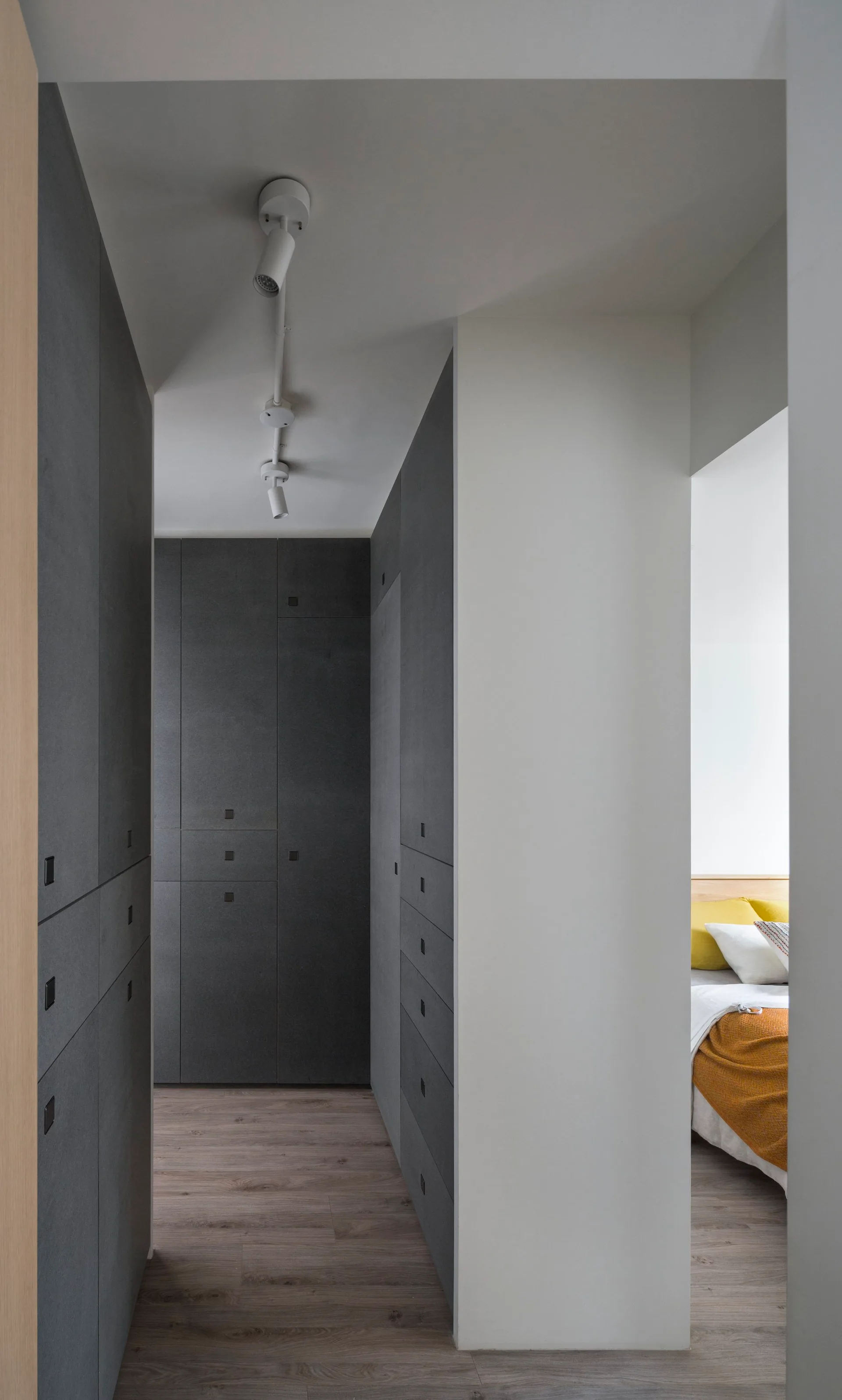 A narrow hallway features built-in dark grey cabinetry and ceiling track lighting with a doorway looking into a bedroom.