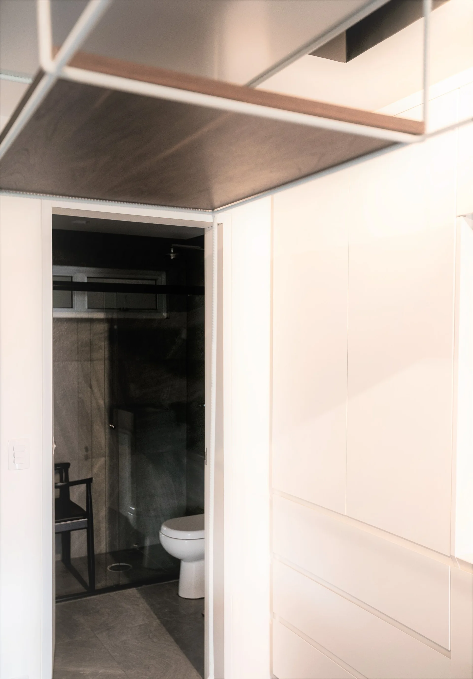 A view through a white doorway reveals a bathroom with grey tiles and a toilet, positioned next to minimalist handleless white cabinets in a hallway.