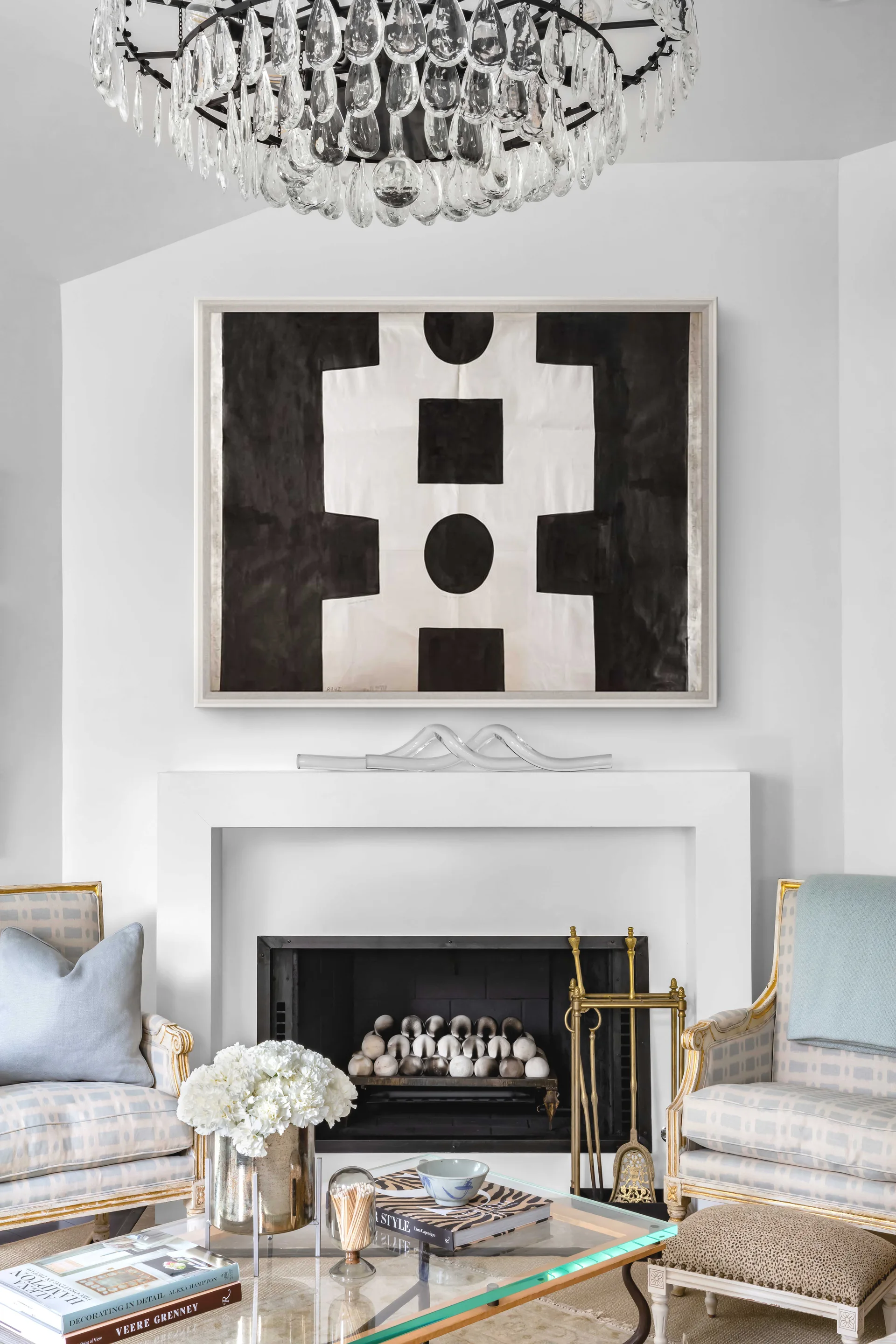 A bright living room fireplace featuring a clean white mantel, high-contrast abstract artwork, and classic upholstered armchairs.