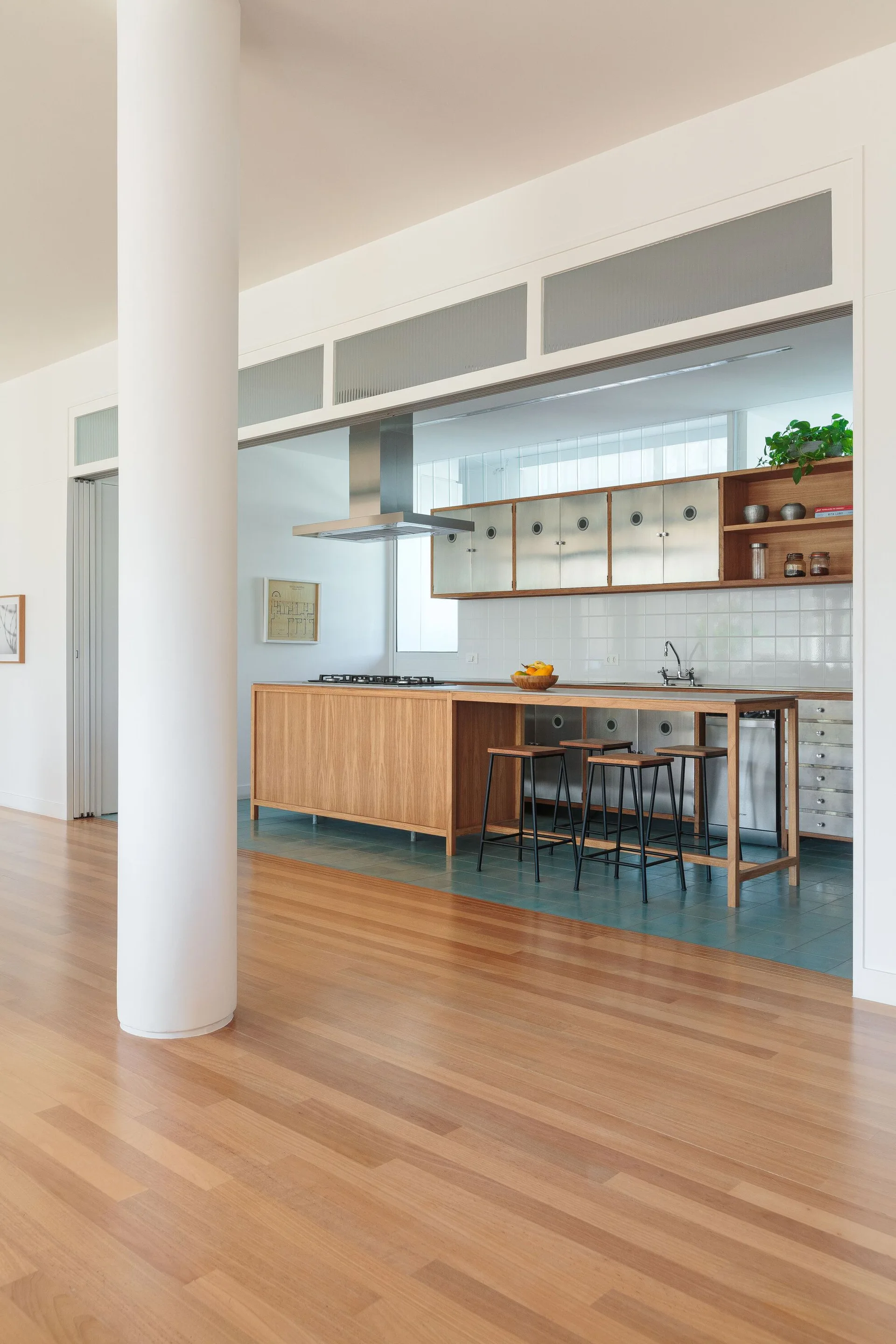 A modern kitchen featuring a wood island with bar stools, stainless steel upper cabinets, and a transition from wood flooring to teal tiles.