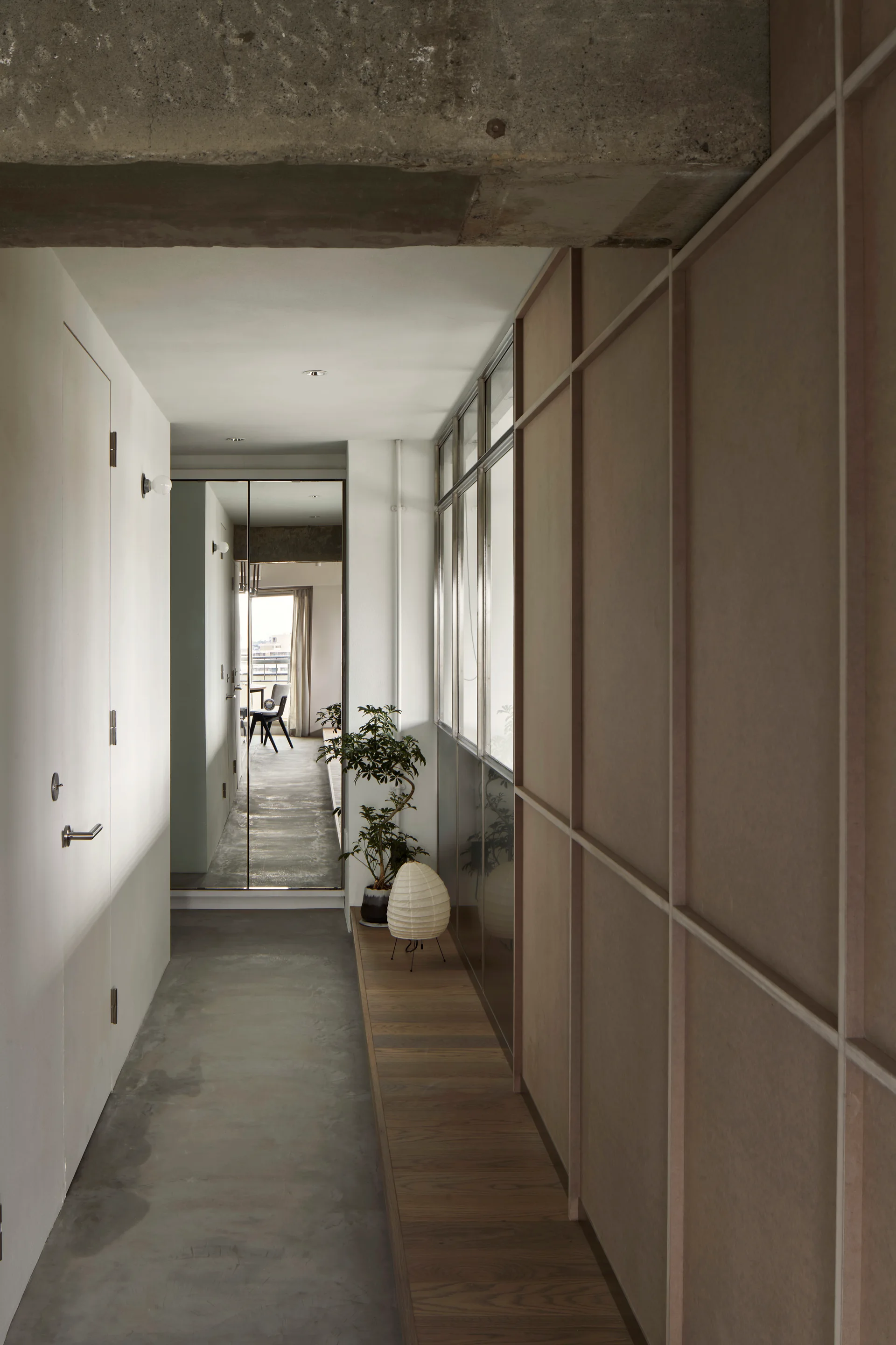 A minimalist interior hallway with polished concrete floors, an exposed concrete ceiling, a wood grid wall, and a low platform shelf.