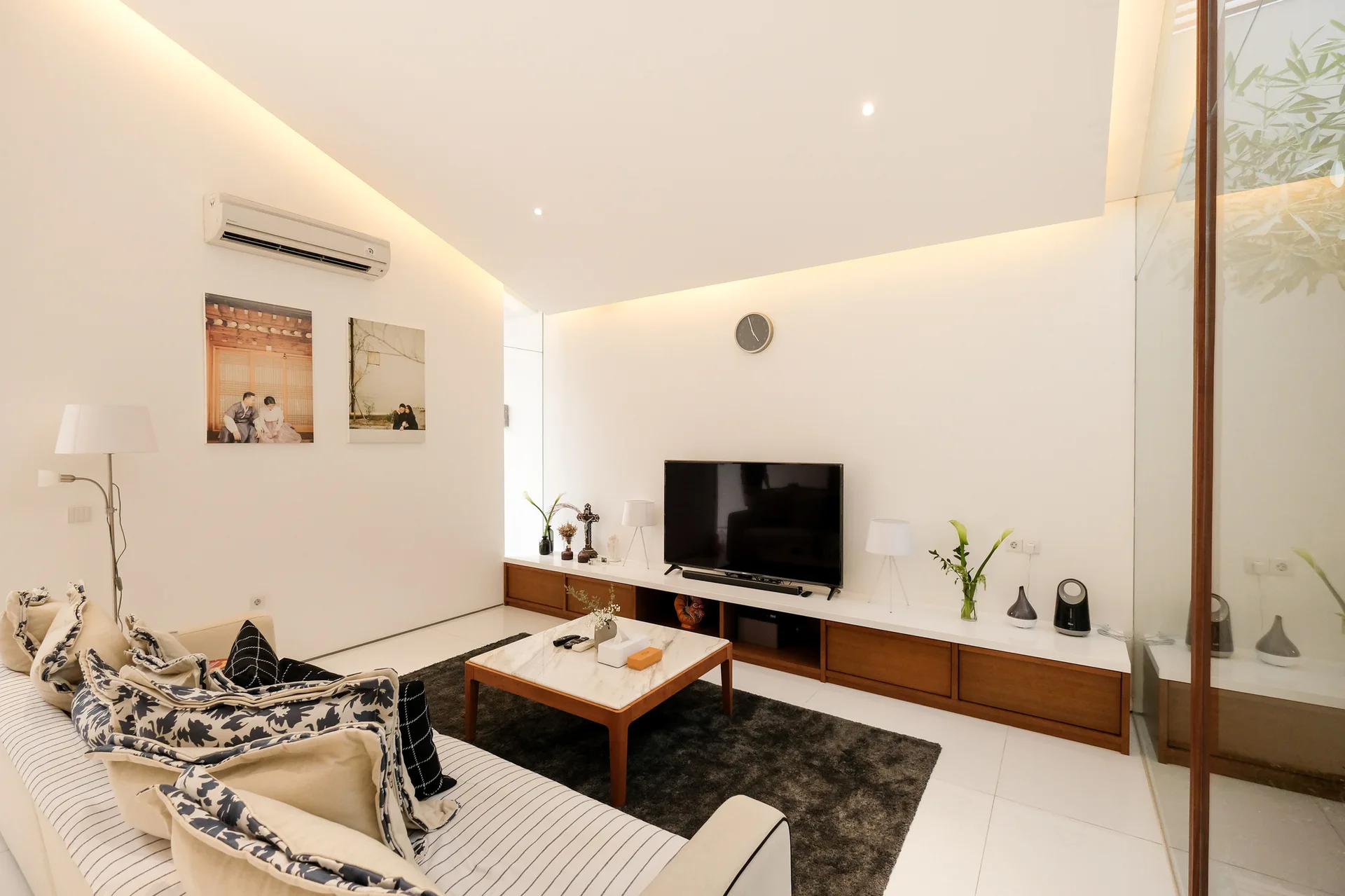 Minimalist living room featuring a striped sofa, marble-top coffee table, and a long wooden media console under an angled ceiling with soft lighting.