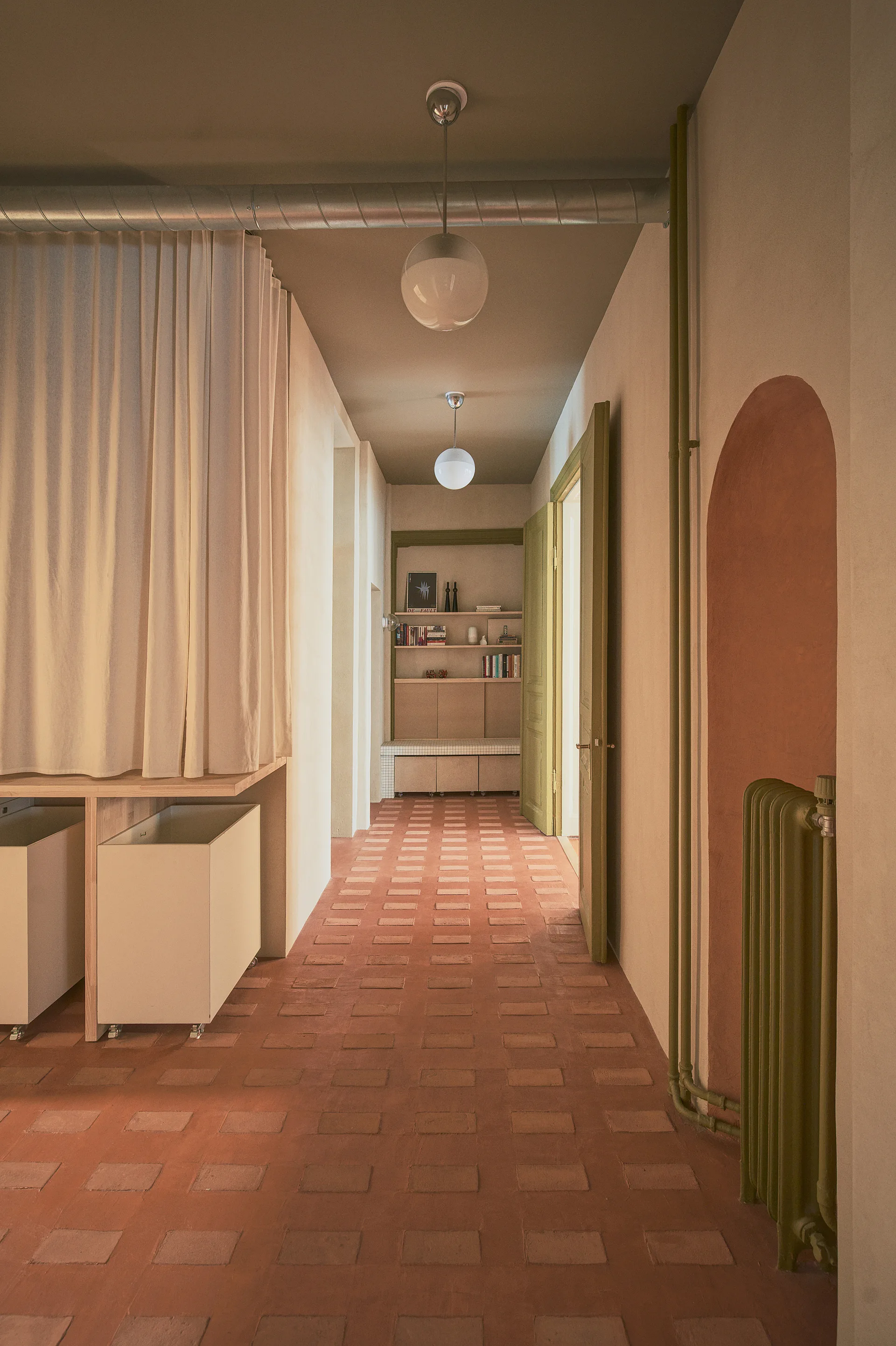 A minimalist hallway features terracotta tile flooring, globe pendant lights, a floor-to-ceiling curtain, and an arched wall alcove.
