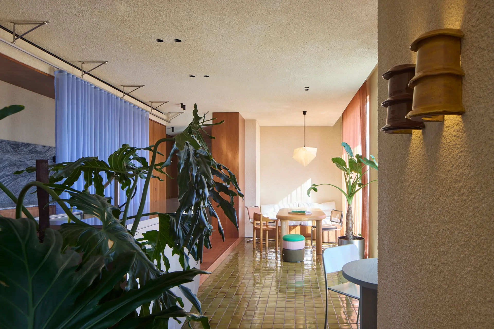 A modern apartment dining area features a wood dining table, brown ceramic floor tiles, textured plaster walls, and a blue partition curtain.