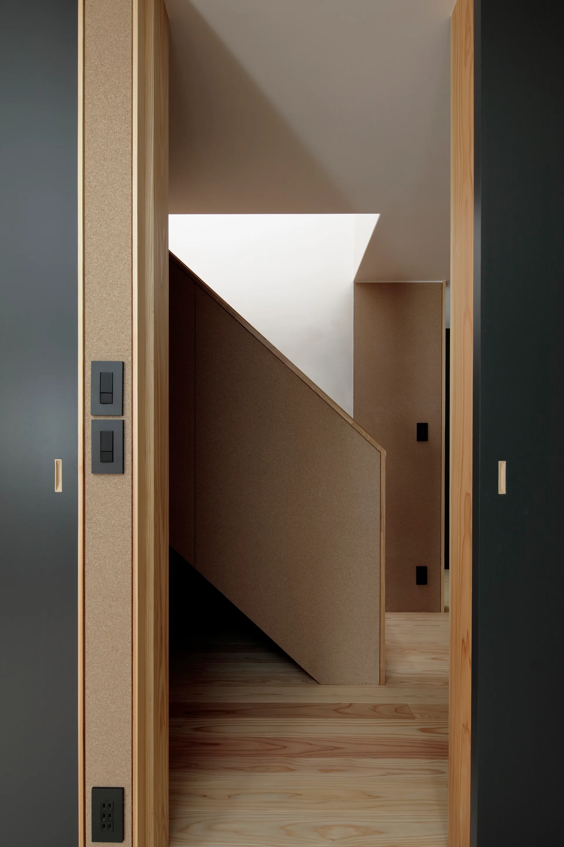 A minimalist entryway framed by charcoal grey sliding doors opens to a natural wood staircase and light plank flooring.