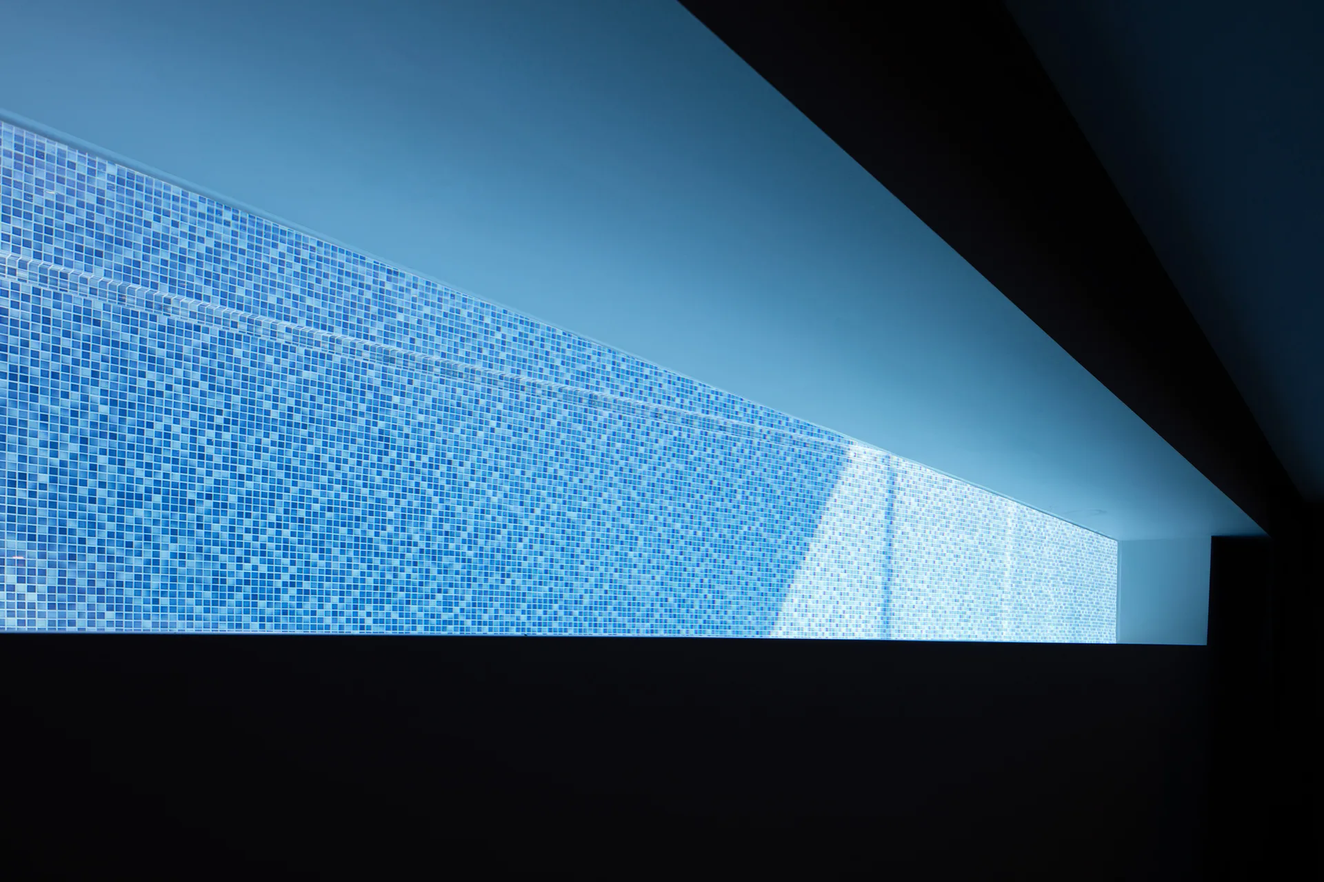 A close-up view of a long, deeply recessed rectangular wall niche lined with small blue mosaic tiles under high-contrast lighting.