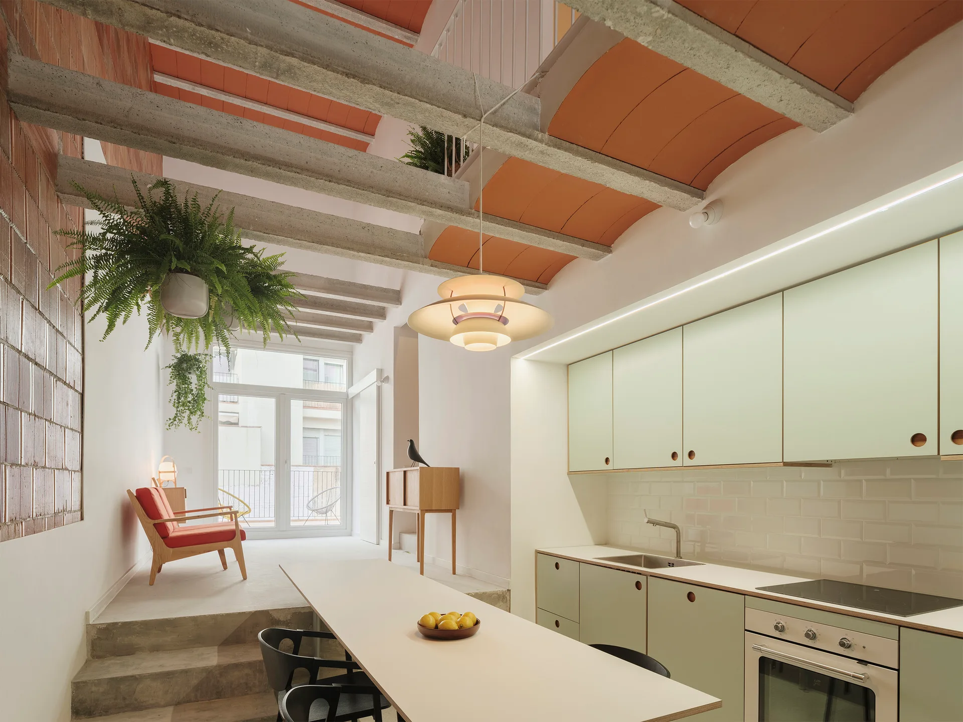 A split-level kitchen featuring pale green cabinetry, a white dining table, and a vaulted terracotta ceiling with concrete beams.