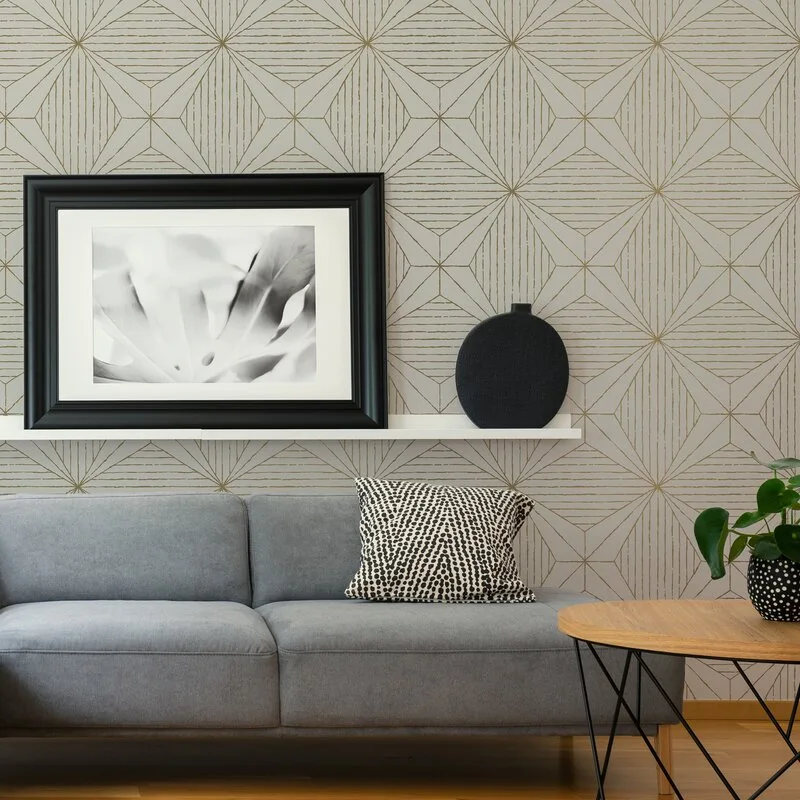 A grey sofa sits in front of geometric wallpaper with a white picture ledge holding a framed black and white photograph.