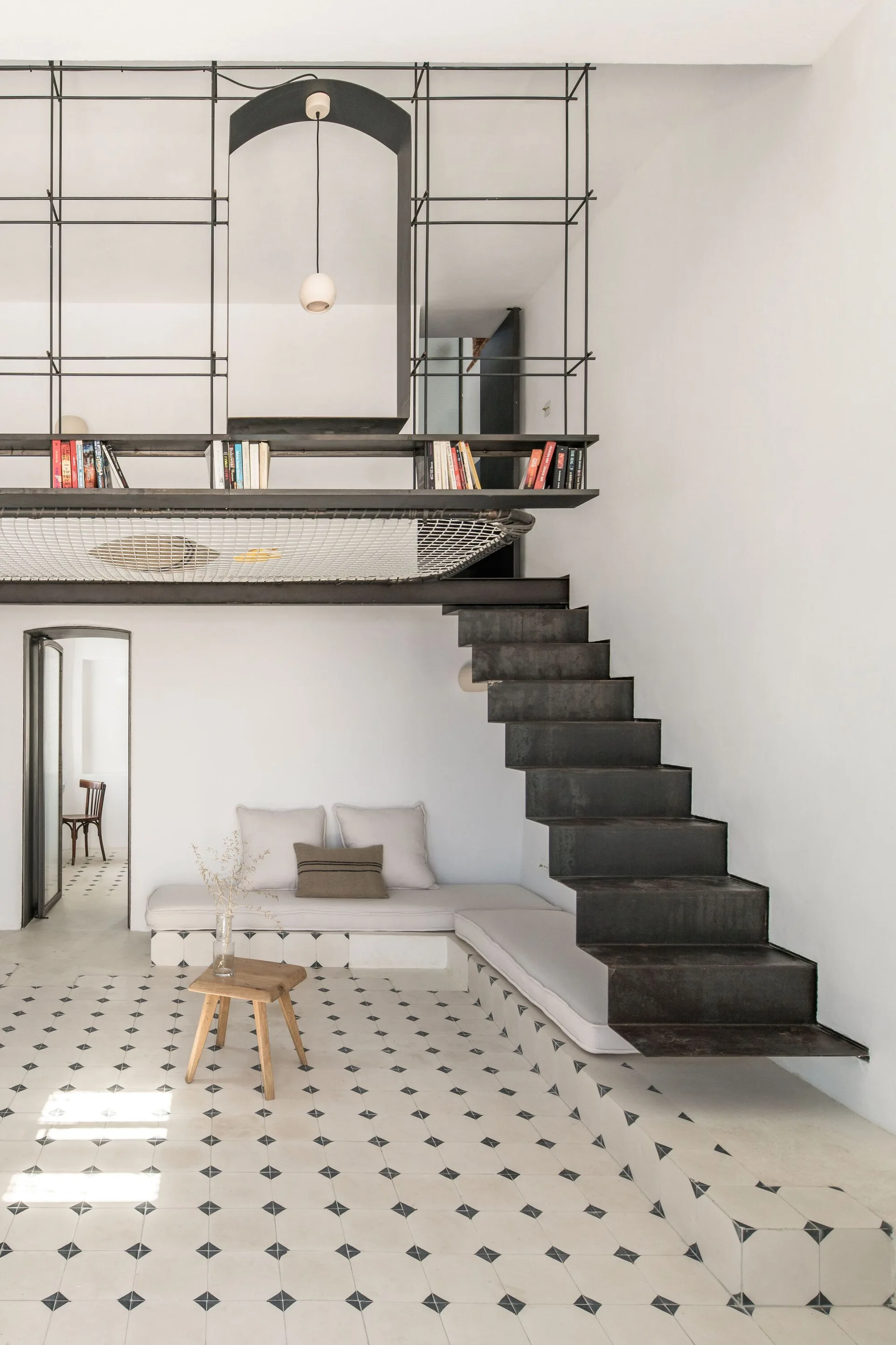 A black floating metal staircase rises alongside a white wall above a built-in corner bench and geometric patterned tile floor.