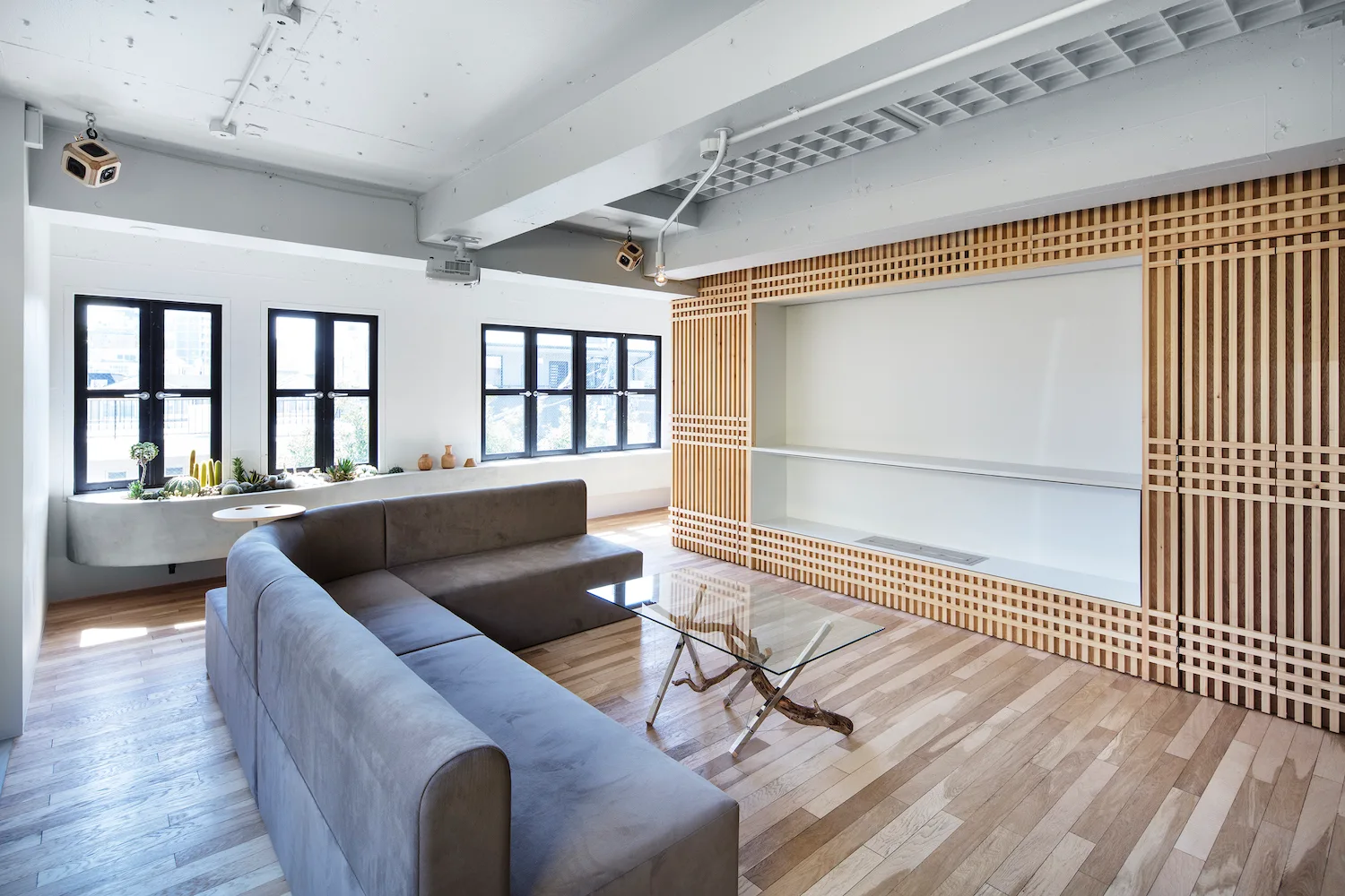 A minimalist living room features a grey sectional sofa, a glass coffee table with a driftwood base, and a large custom slatted wood wall unit.