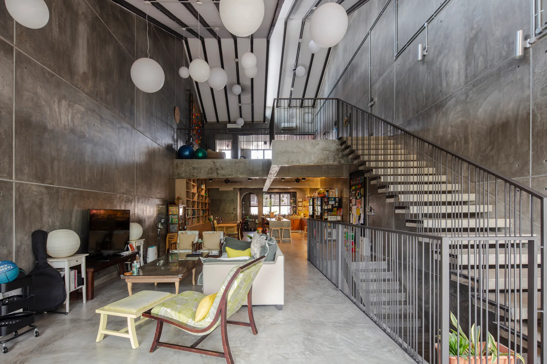 A double-height living room features polished concrete walls, a metal staircase, and multiple white globe pendant lights hanging from the ceiling.