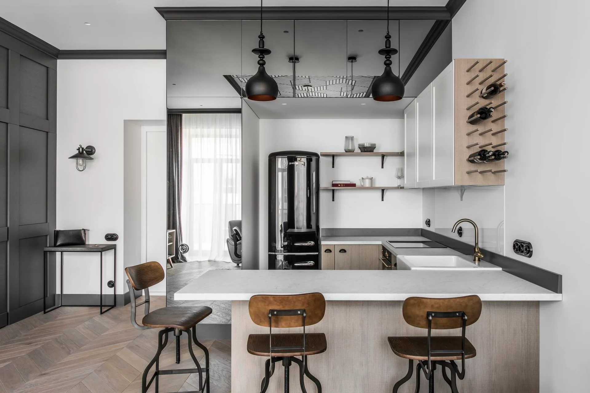 A modern kitchen featuring a stone-topped island with wood bar stools, a black retro refrigerator, and a reflective mirrored wall.