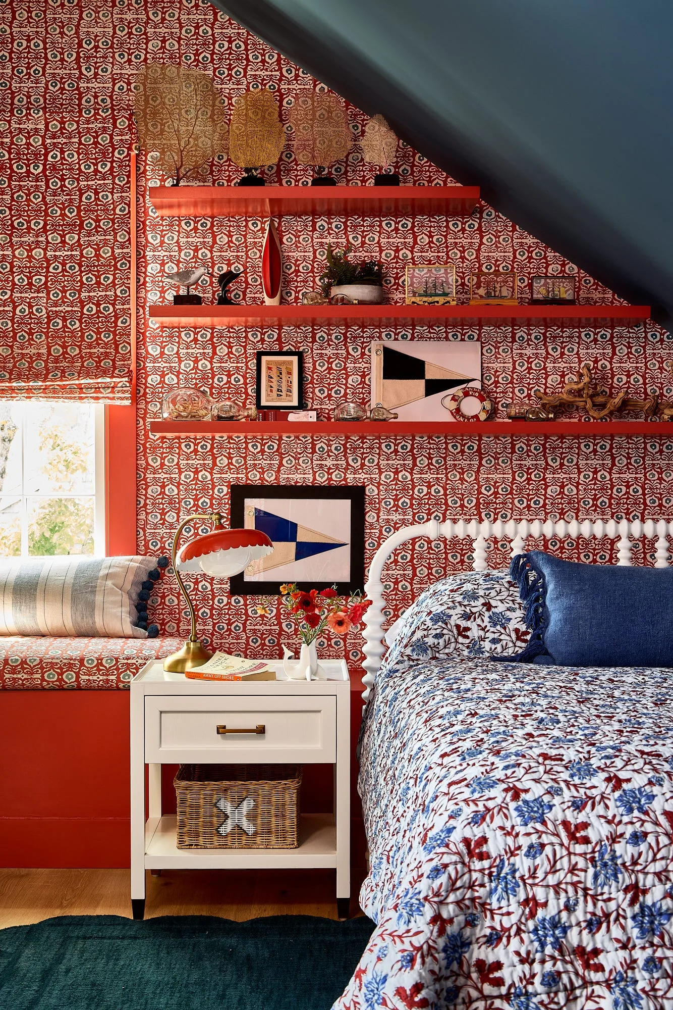 A bedroom corner features red patterned wallpaper, matching red floating shelves on a sloped wall, a white nightstand, and a spindle bed.